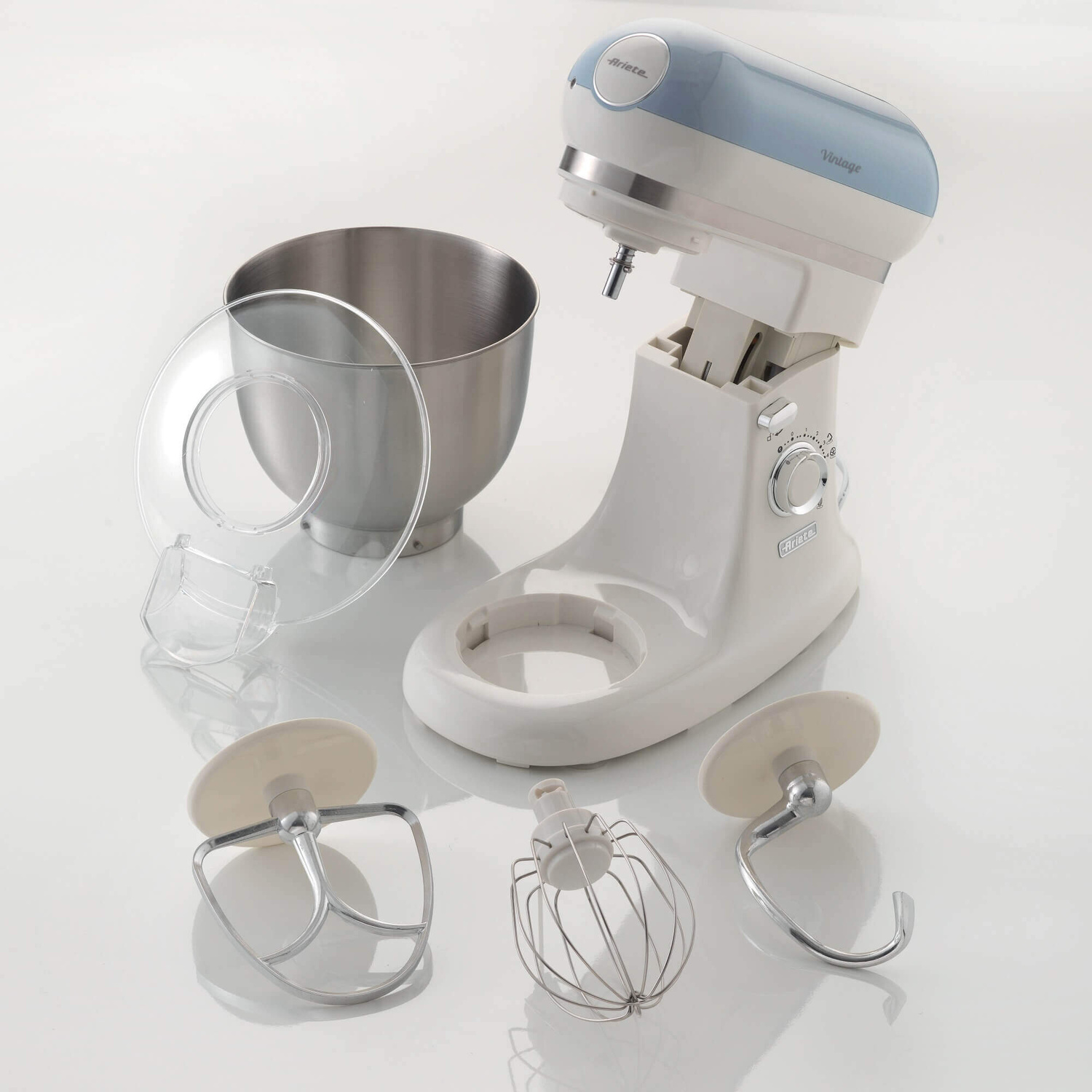 Un'impastatrice bianca e blu con ciotola in acciaio inox, paraschizzi e tre accessori su fondo bianco.