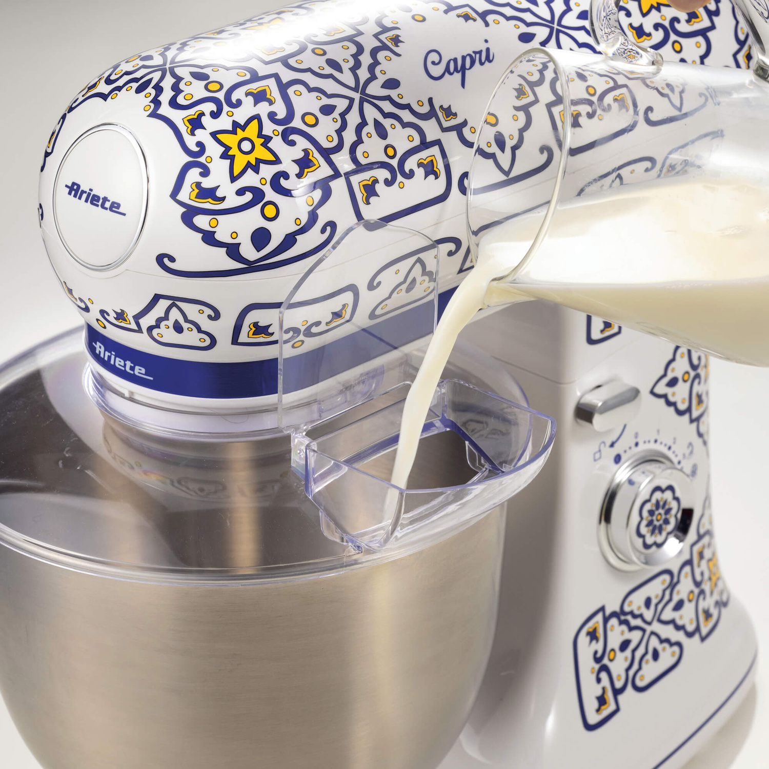 Il latte viene versato in un'elegante impastatrice bianca Ariete Capri con motivo blu e giallo.