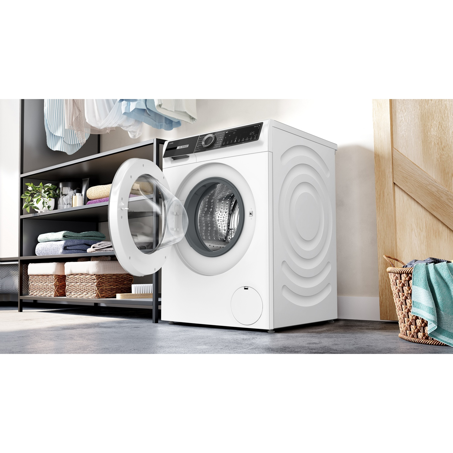 Een witte wasmachine met open deur staat in een wasruimte naast planken met handdoeken en een mand.