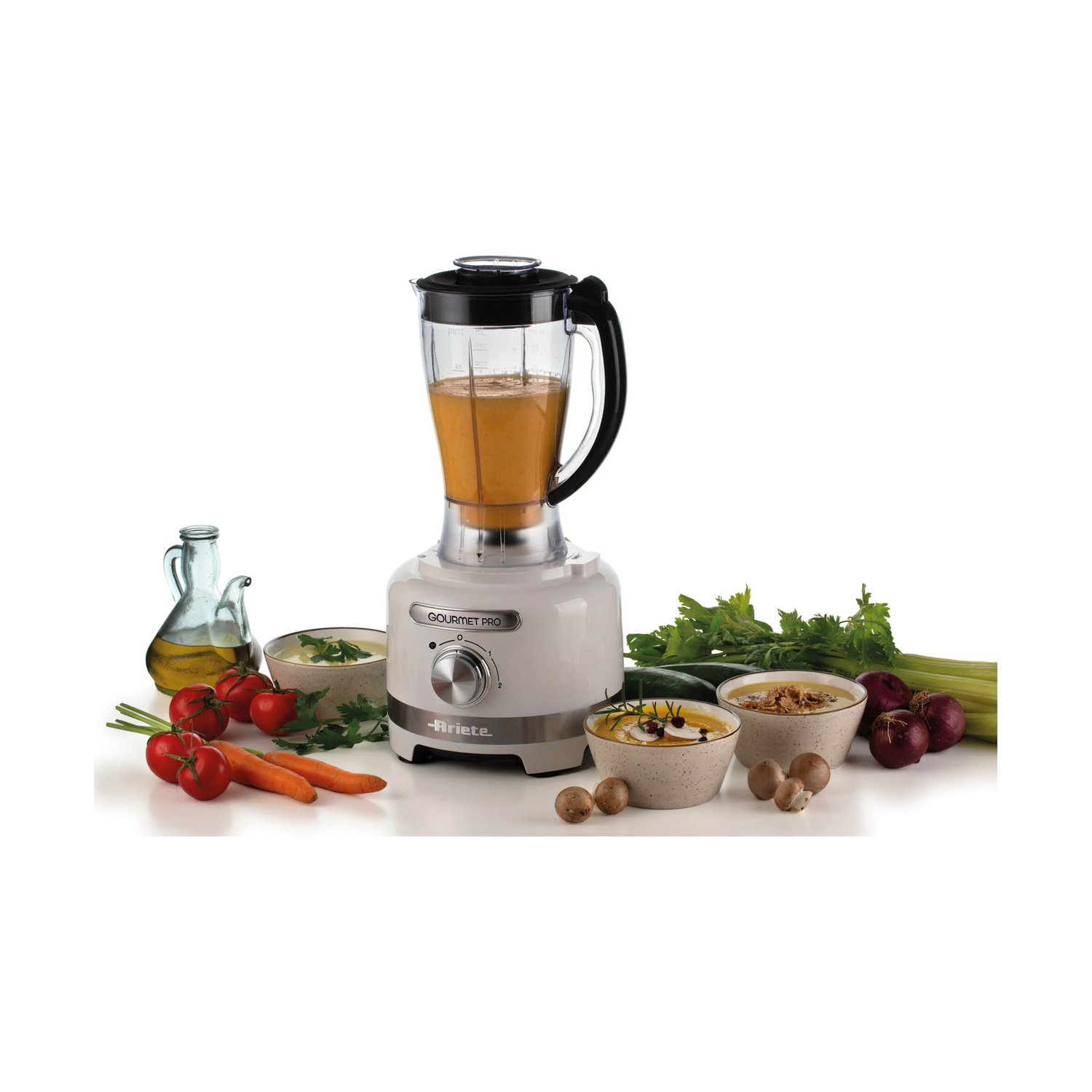 Un frullatore bianco Gourmet Pro è circondato da ingredienti freschi come pomodori, carote e funghi.