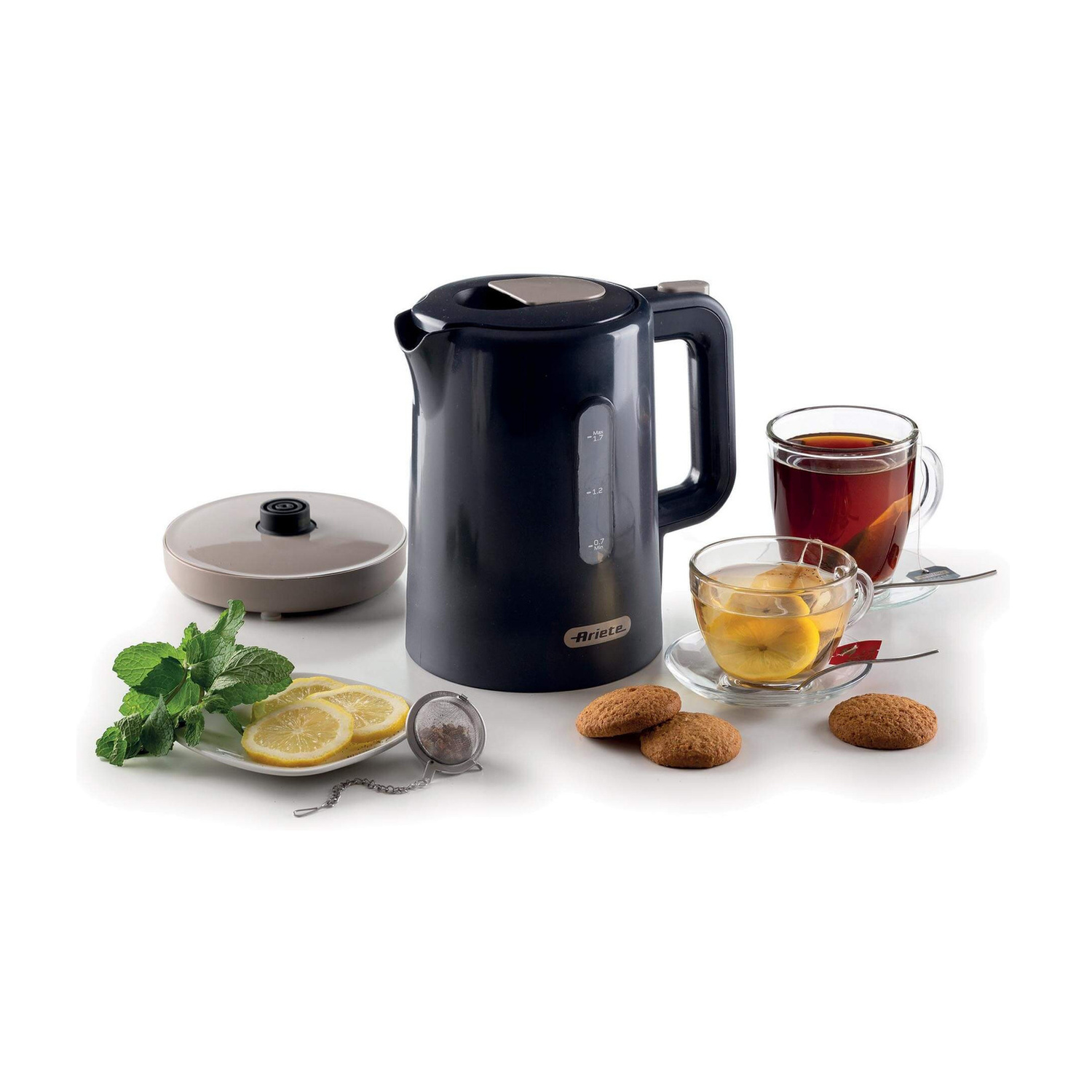 Un bollitore elettrico nero, tazze di tè con limone, un piatto di menta e fette di limone, un colino e biscotti.