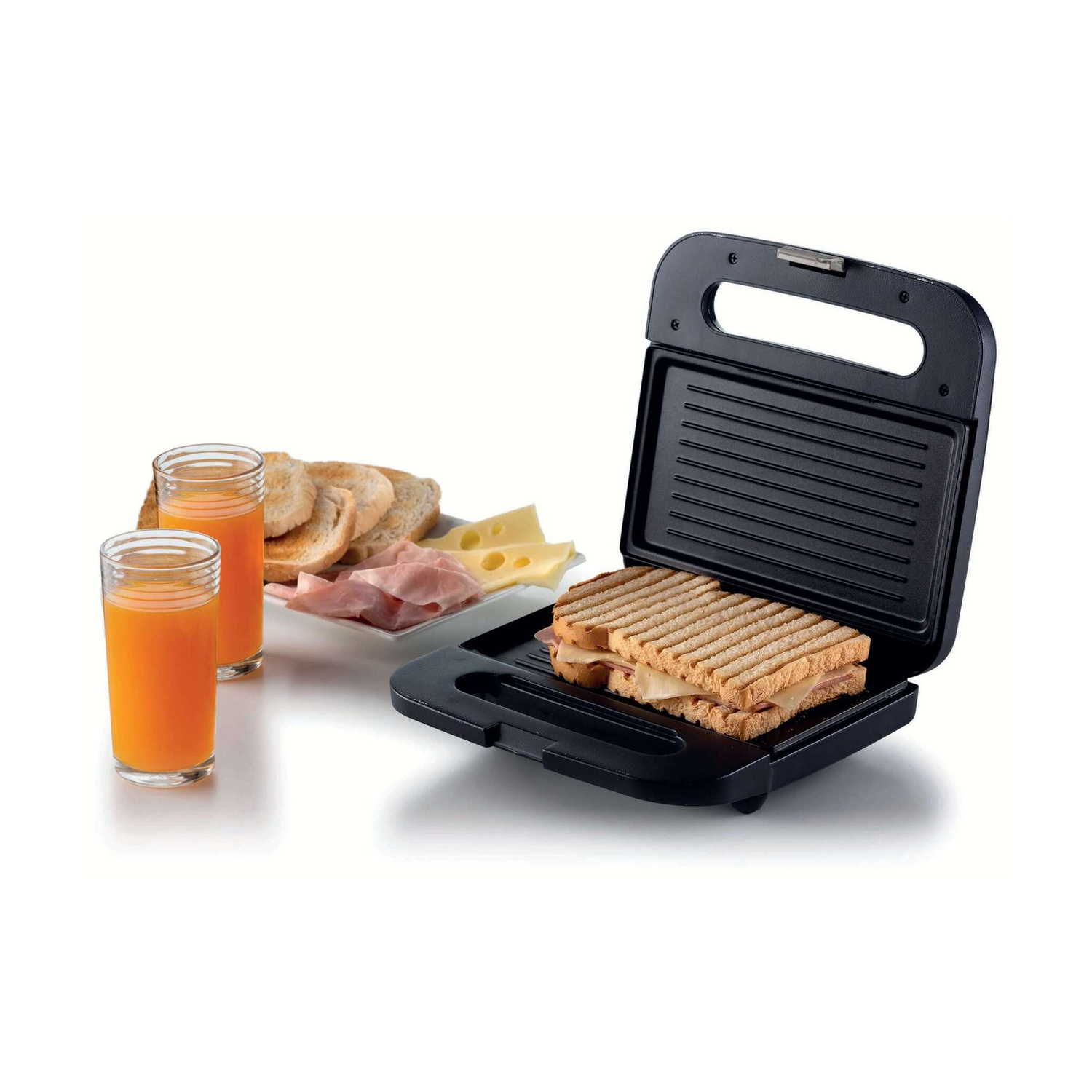 Una piastra per panini nera con un toast grigliato, accanto a pane tostato, prosciutto, formaggio e due bicchieri di succo.