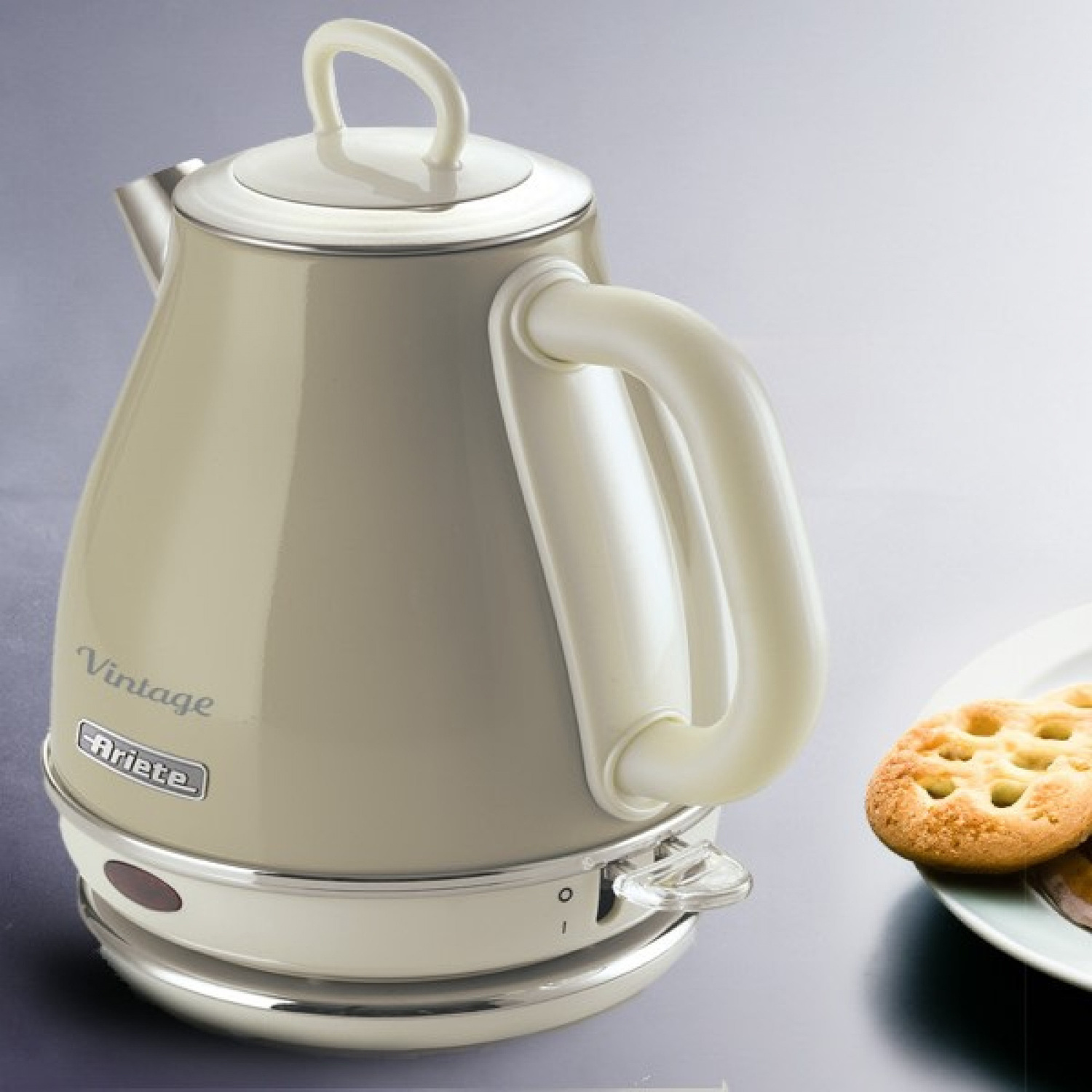 Un bollitore elettrico vintage beige Ariete su una superficie grigia, con un biscotto su un piatto a destra.