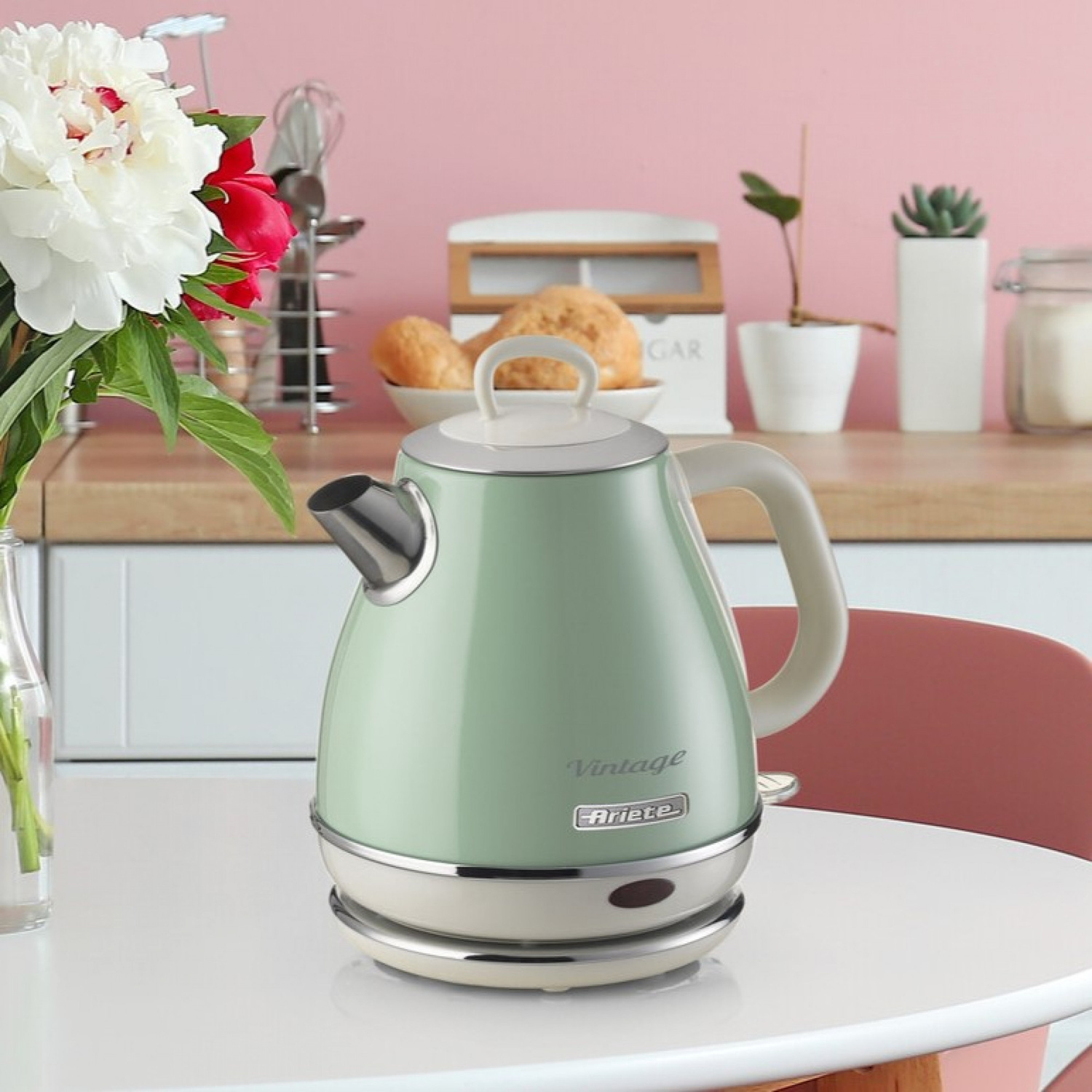 Un bollitore vintage Ariete verde pastello su un tavolo bianco in cucina con fiori in primo piano.