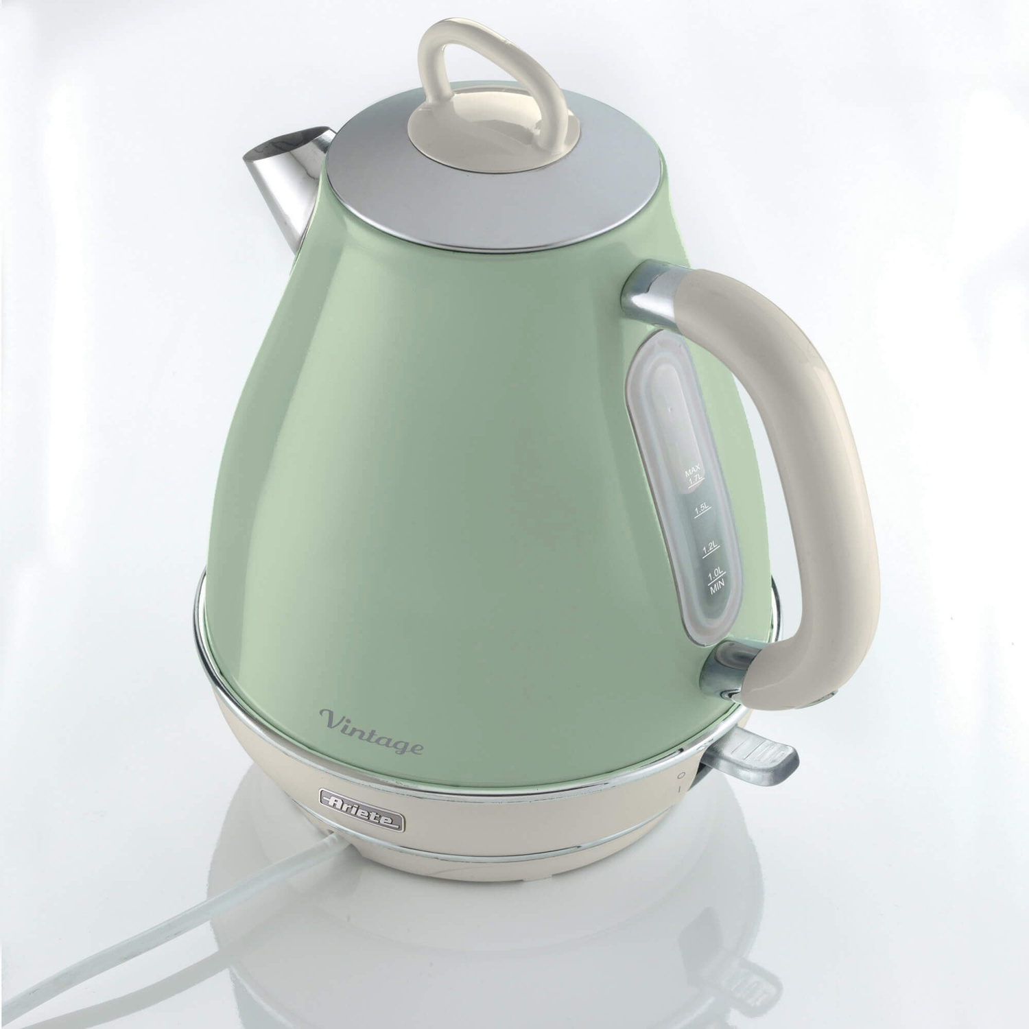 Un bollitore elettrico vintage verde pastello con manico e base crema su superficie bianca.