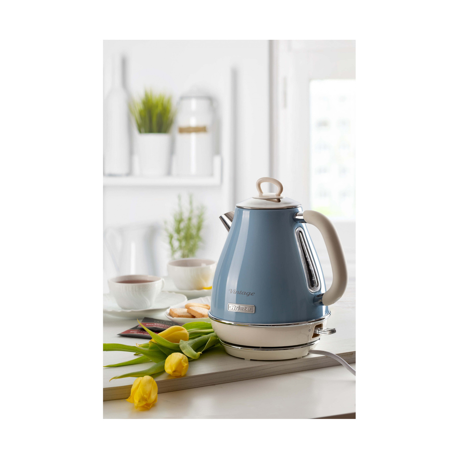 Un bollitore elettrico vintage blu Ariete su un bancone da cucina con tulipani gialli e tazze.