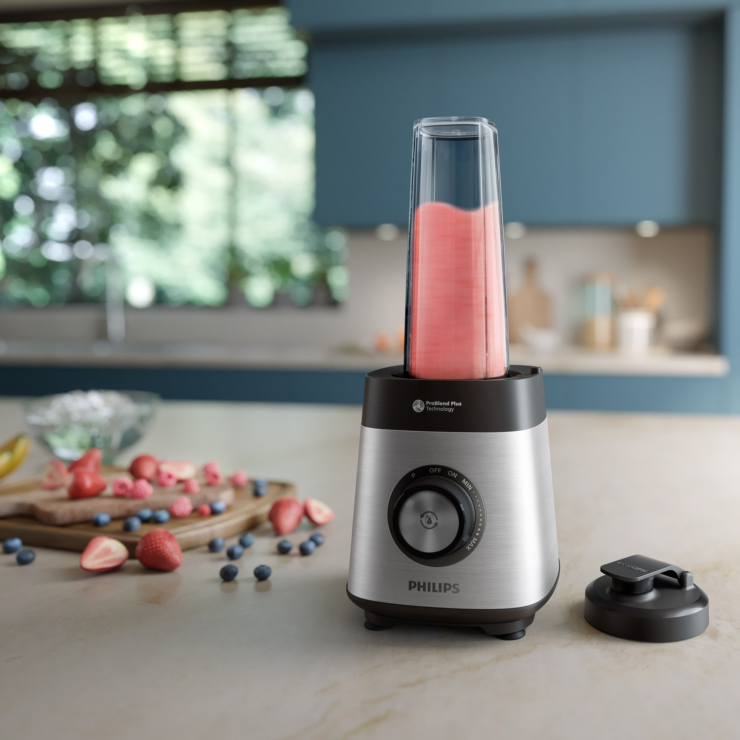 Un blender Philips argenté sur un comptoir avec un smoothie rose et des baies éparpillées.