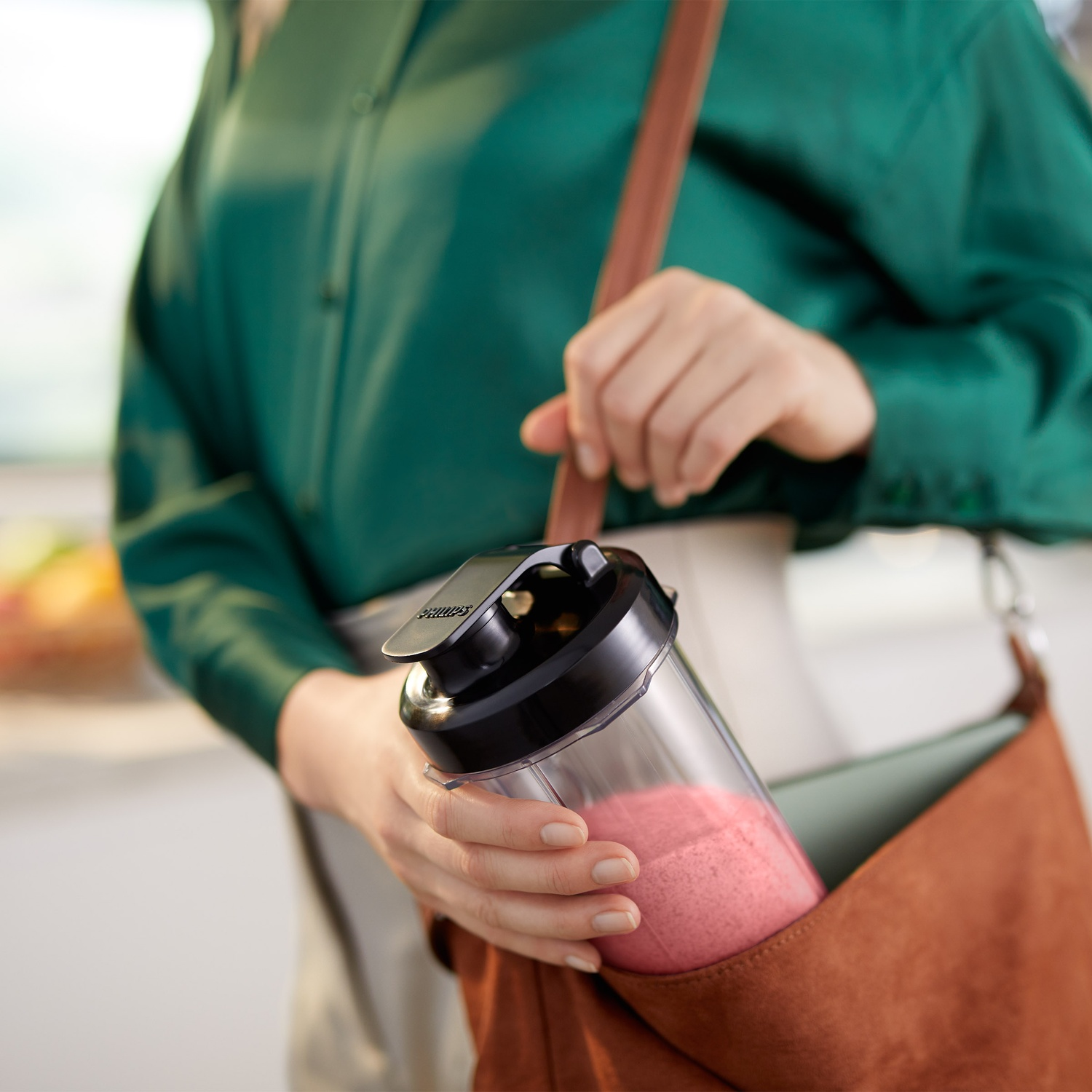 Une femme en chemise verte met une bouteille de smoothie rose dans un sac marron.
