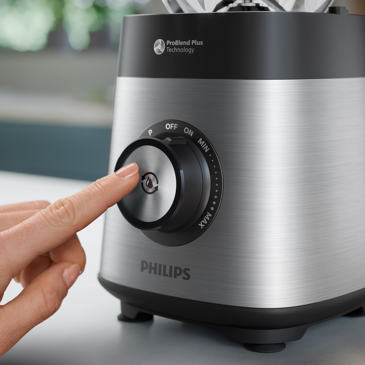 Une main touche le bouton de commande d'un mixeur Philips argenté.