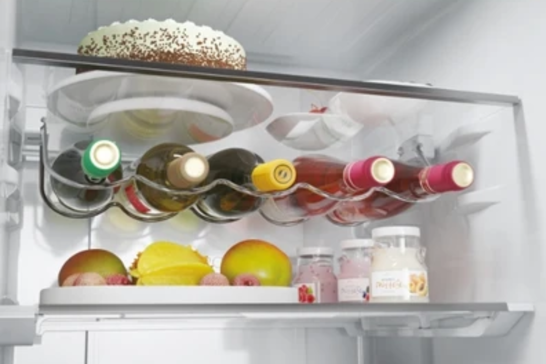 Un estante de refrigerador con un pastel arriba, botellas de vino en el medio y fruta y frascos abajo.