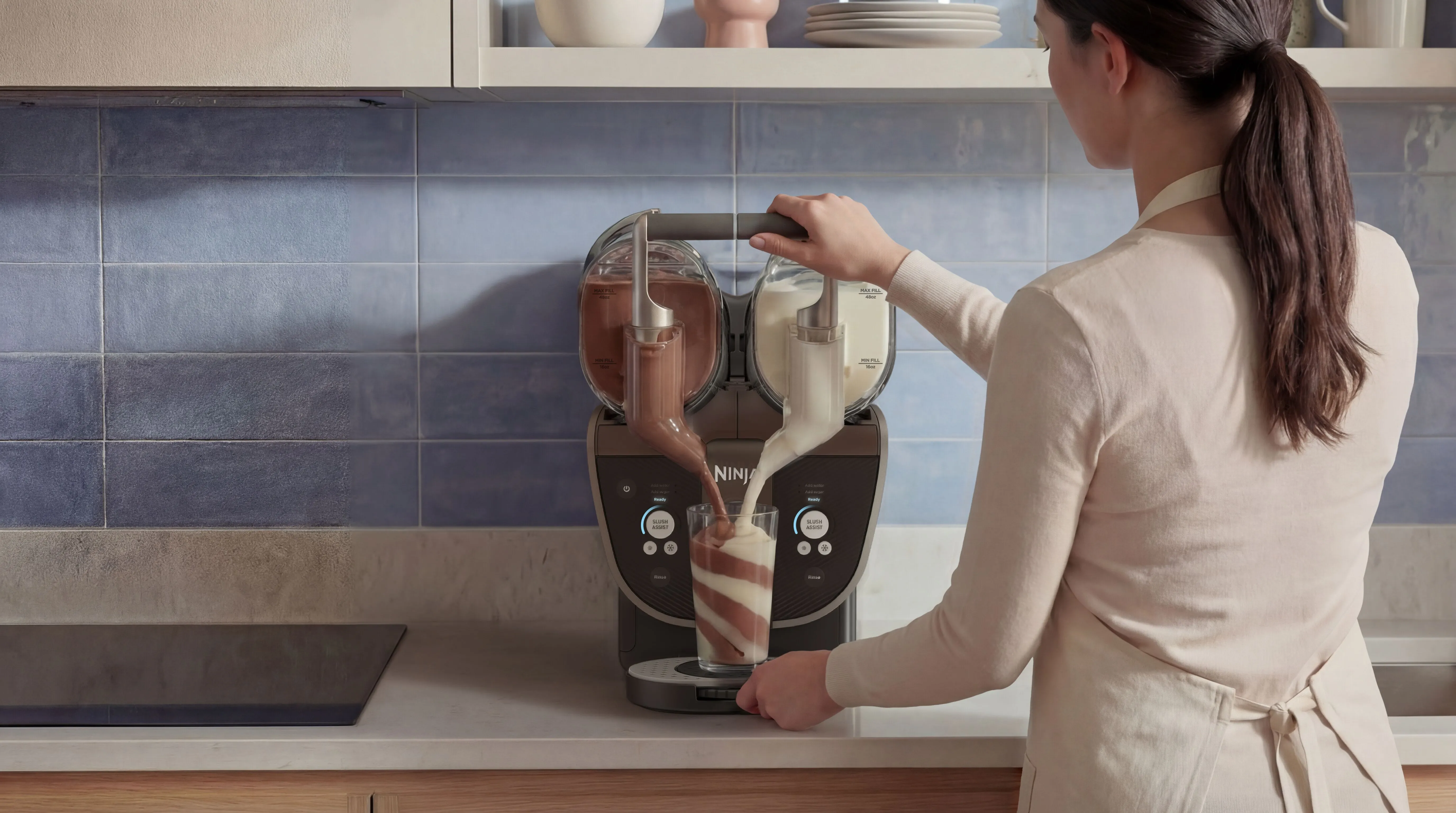 Eine Frau bedient eine Ninja-Maschine, die Schoko- und Vanilleeis in ein Glas gießt.
