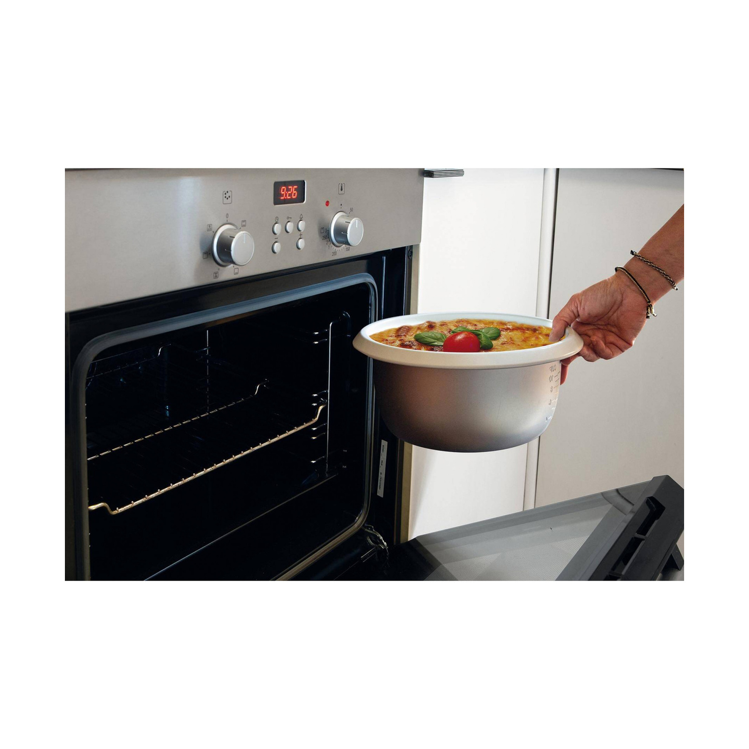 Una persona inserisce una pentola rotonda con del cibo in un forno aperto in acciaio inossidabile.
