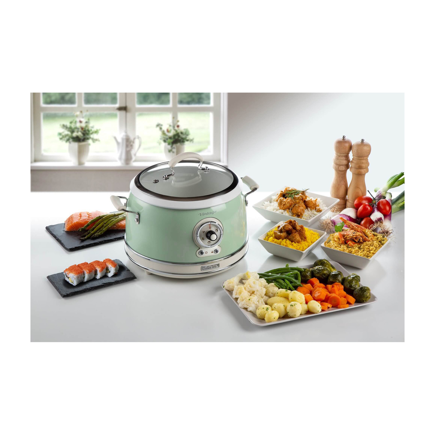 Un cuoco multifunzione verde menta su un tavolo, circondato da vari piatti preparati e ingredienti freschi.