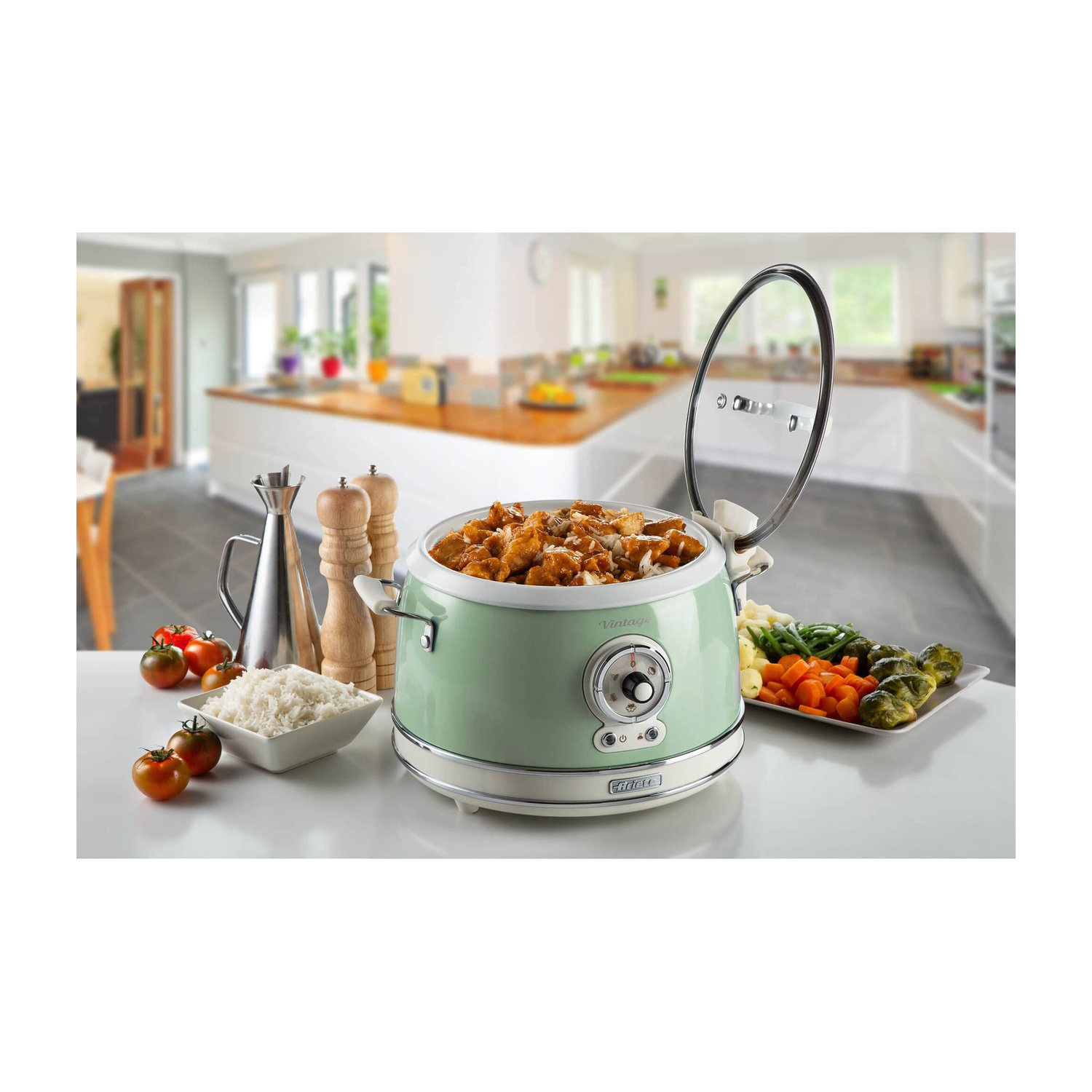 Un multicooker verde menta sul piano cucina pieno di carne e riso, con coperchio in vetro aperto e contorni.