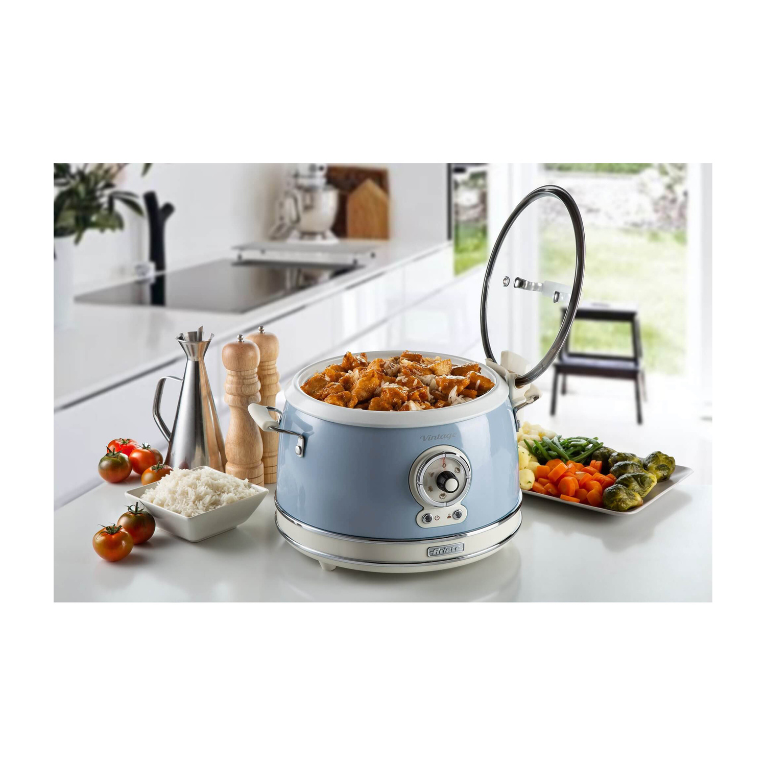 Multicooker vintage azzurro con coperchio aperto su un piano di lavoro, circondato da cibo e utensili.