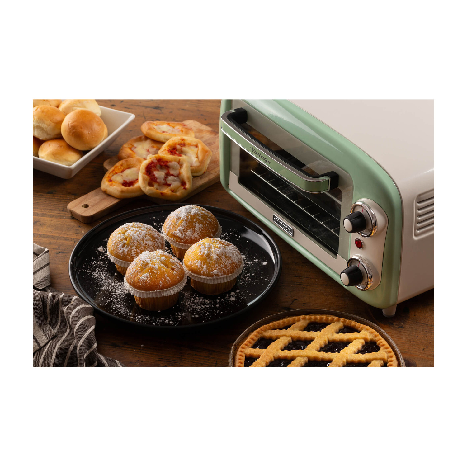 Un mini forno verde menta si trova su un tavolo accanto a muffin, panini, mini pizze e una torta.