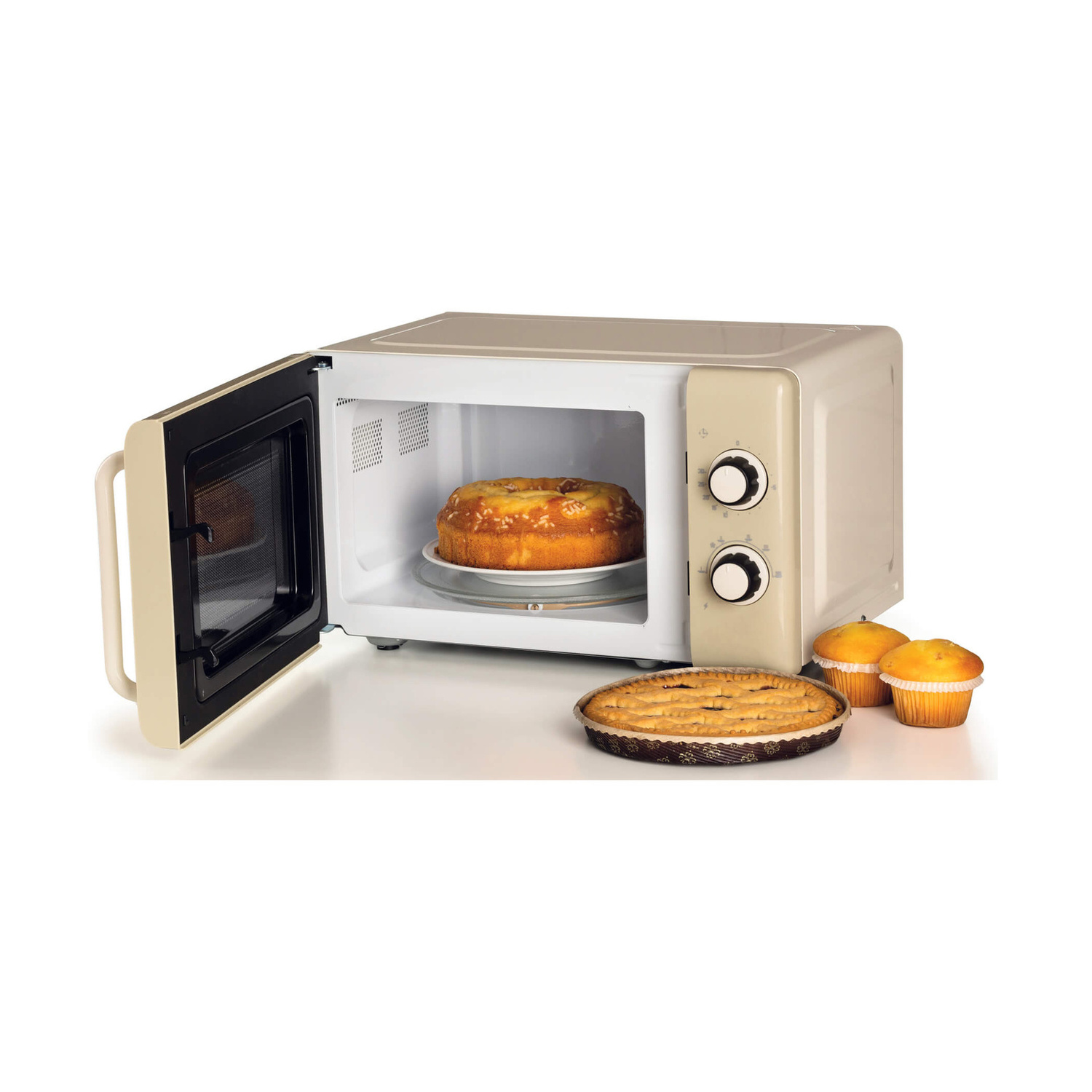 Microonde beige con porta aperta, una torta rotonda dentro, una crostata e muffin sul tavolo.
