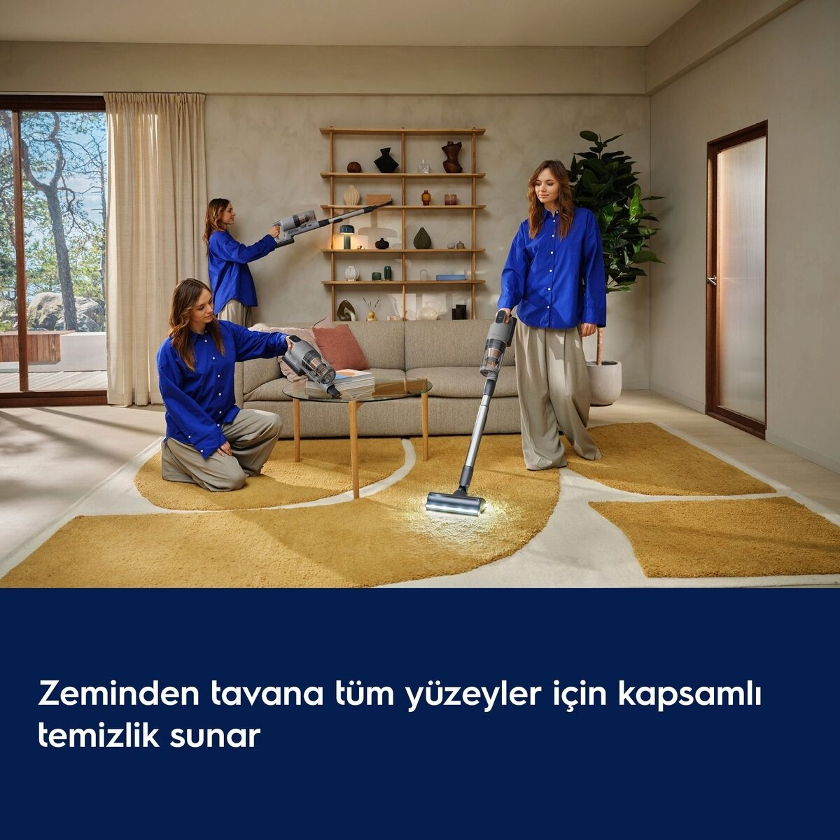 Mavi gömlekli bir kadın, kanepe ve ahşap raflı oturma odasını dikey süpürgeyle temizliyor.