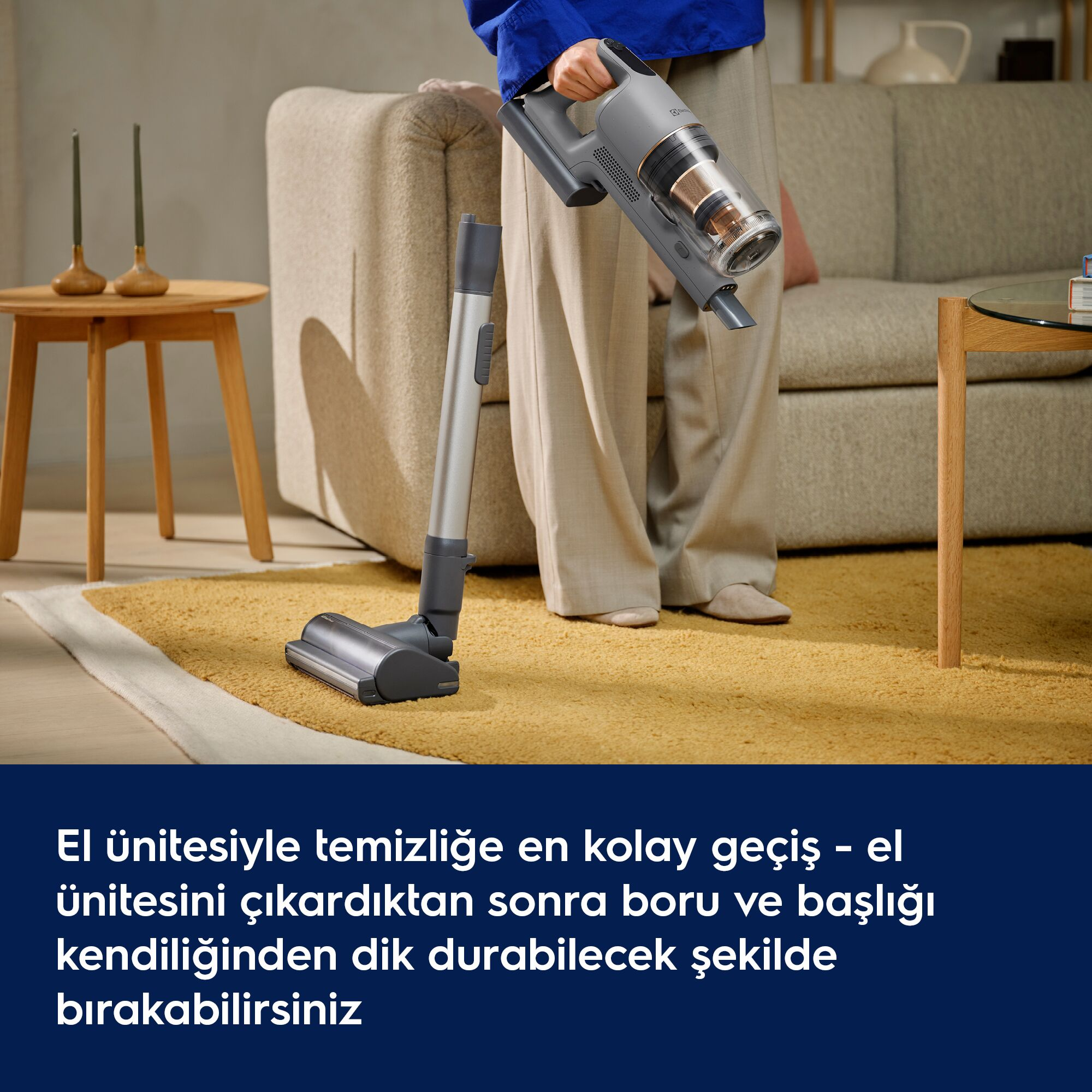Bir kişi, sarı halı üzerinde dik duran yer başlığının üzerinde gri el süpürgesi tutuyor.