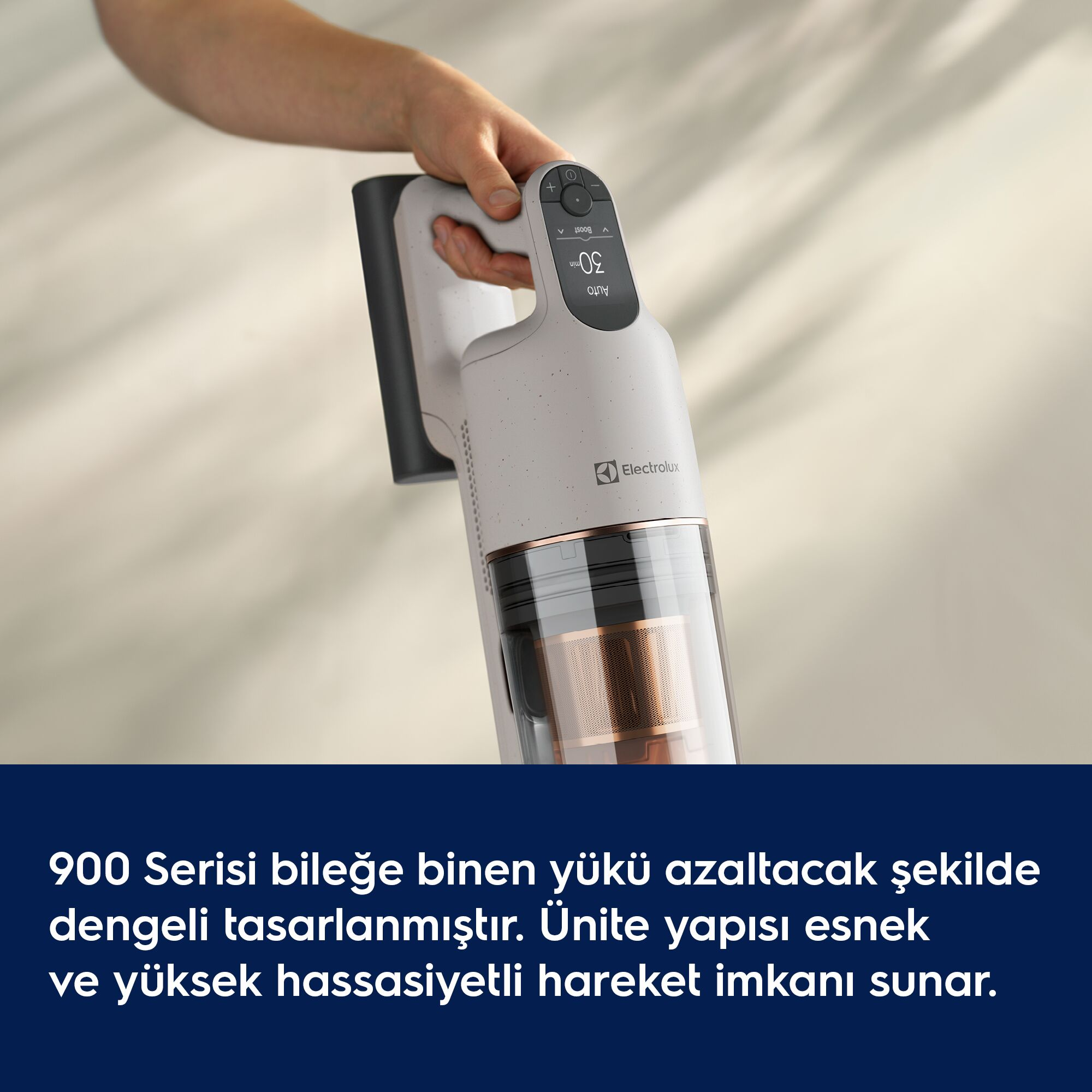 Bir el, açık renkli fon ve alt bant önünde gri Electrolux dikey süpürgeyi tutuyor.