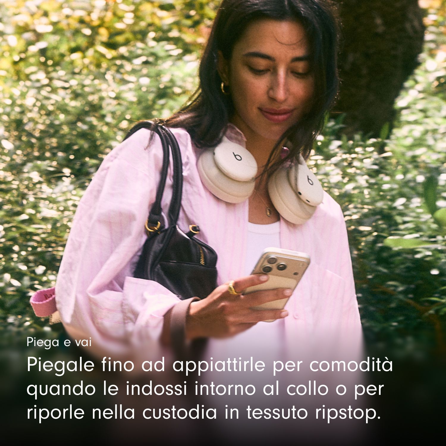 Una donna con camicia rosa guarda il telefono, con cuffie bianche al collo.