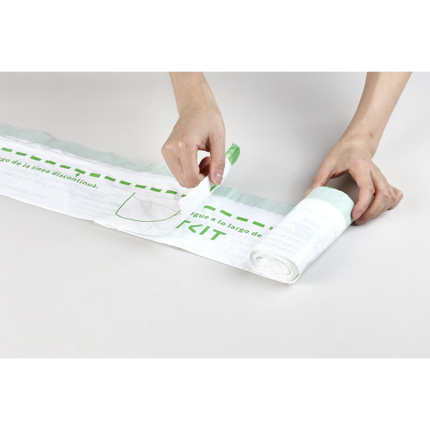 Des mains déroulent un sac en plastique blanc avec du texte vert sur une surface claire.