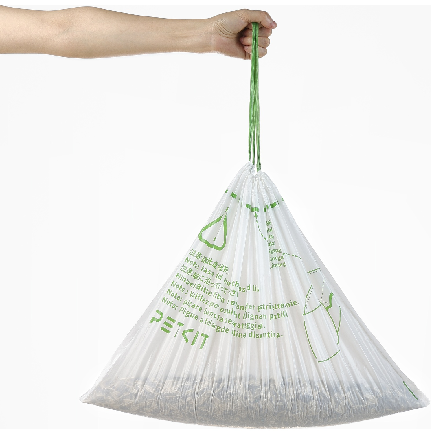 Une main tient un sac poubelle blanc fermé avec des cordons verts et du texte imprimé.