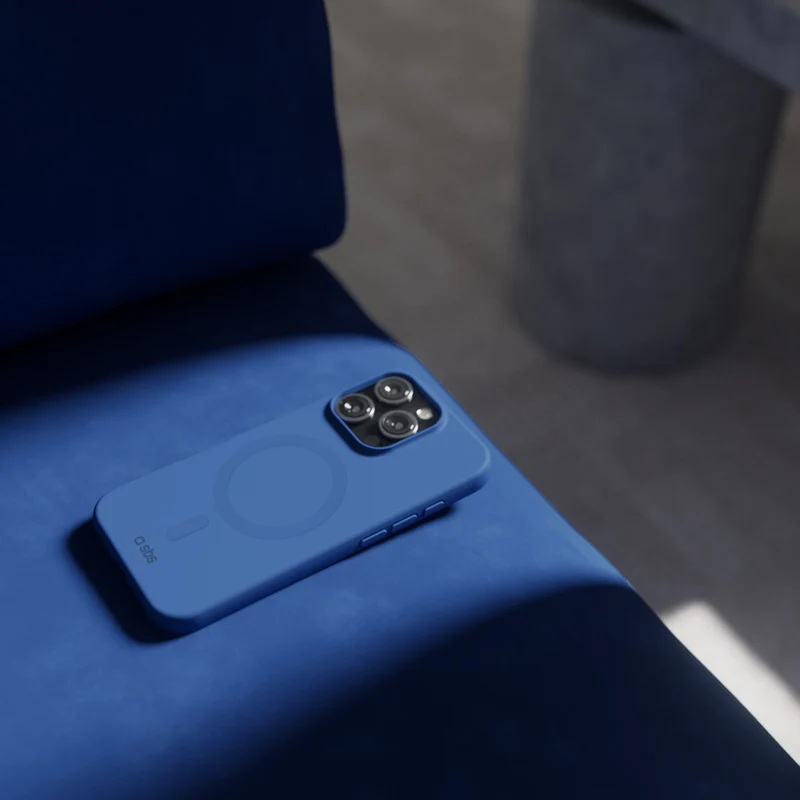 Niebieski smartfon w etui leży na niebieskiej poduszce w ciemnym pokoju.
