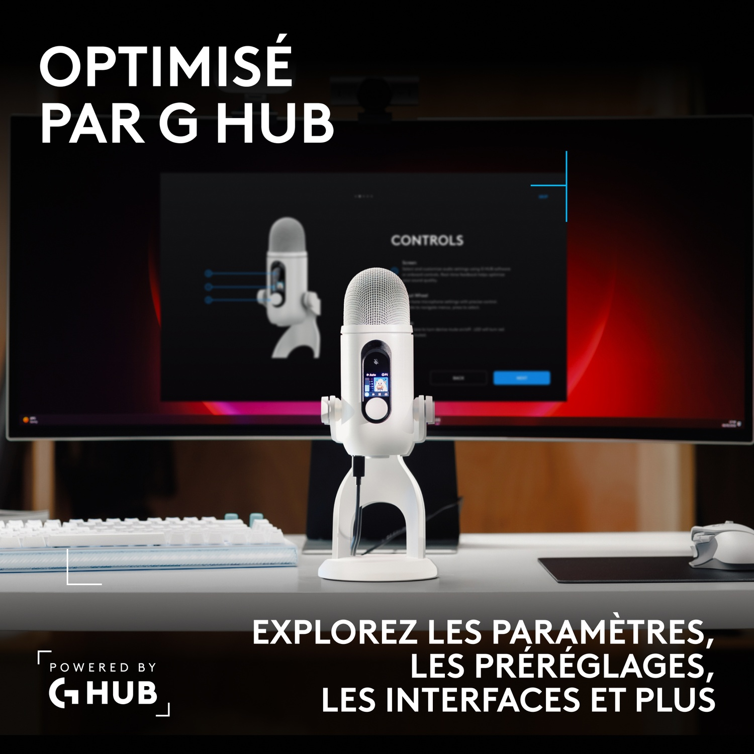 Un microphone blanc posé sur un bureau devant un écran affichant des commandes, avec clavier et souris.