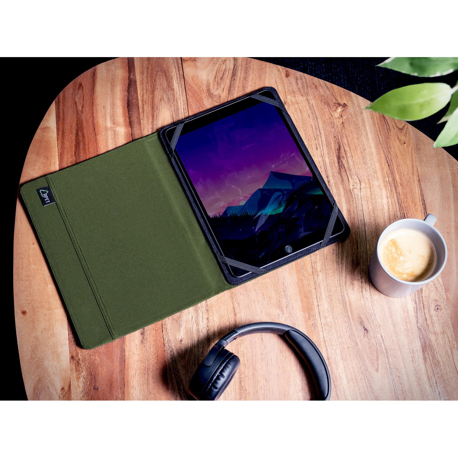 Un tablet in custodia verde, cuffie e tazza di caffè su un tavolo di legno.