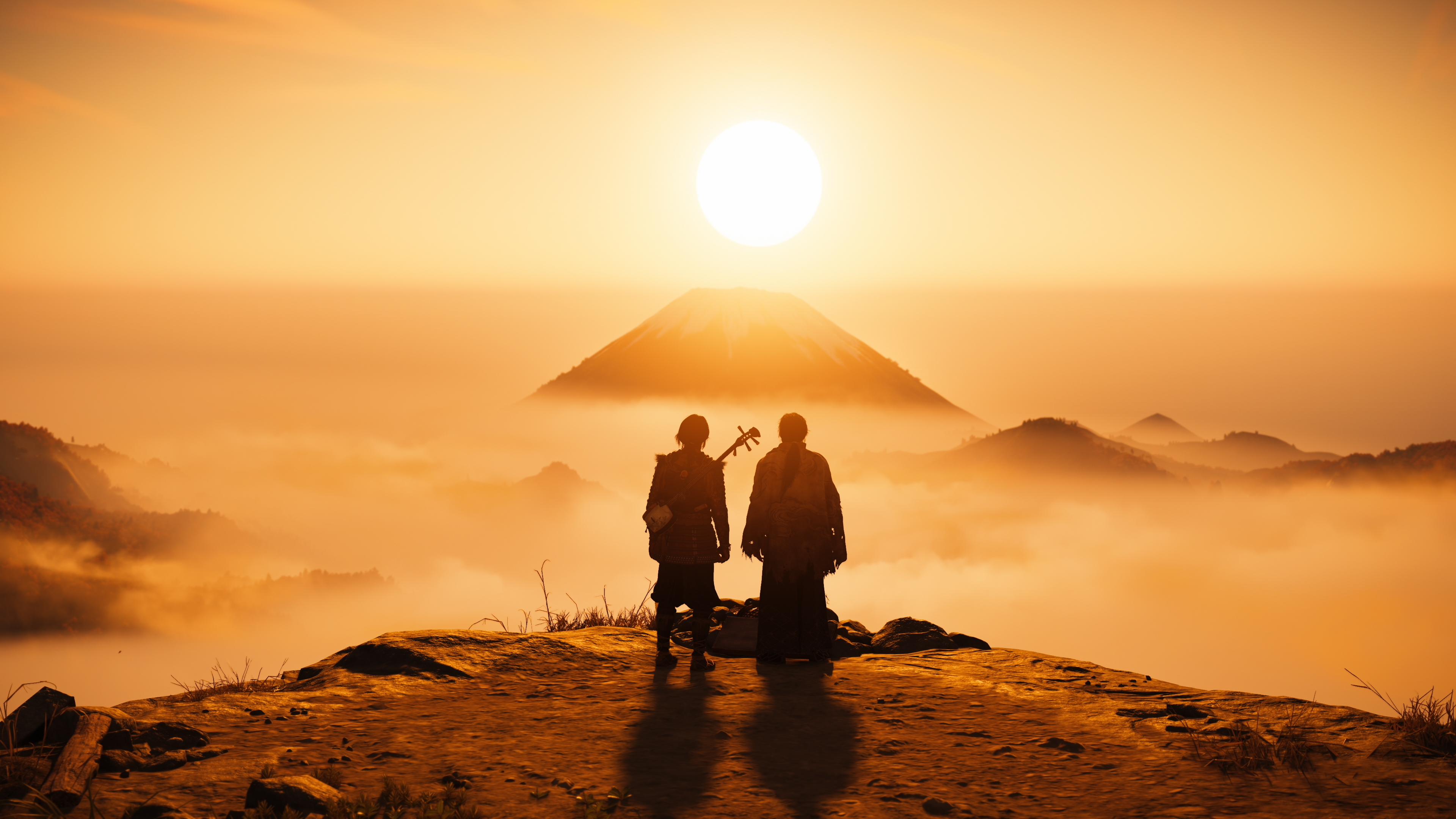 Zwei Personen stehen auf einem Felsen und betrachten bei Sonnenuntergang eine ferne Bergspitze über dem Nebel.