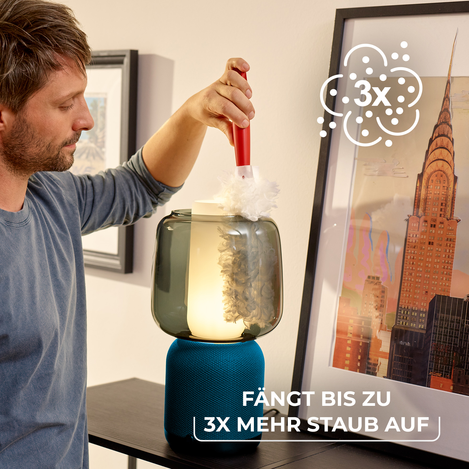 Ein Mann benutzt einen kleinen Staubwedel an einer leuchtenden Lampe mit grauem Glasschirm und blauem Fuß.