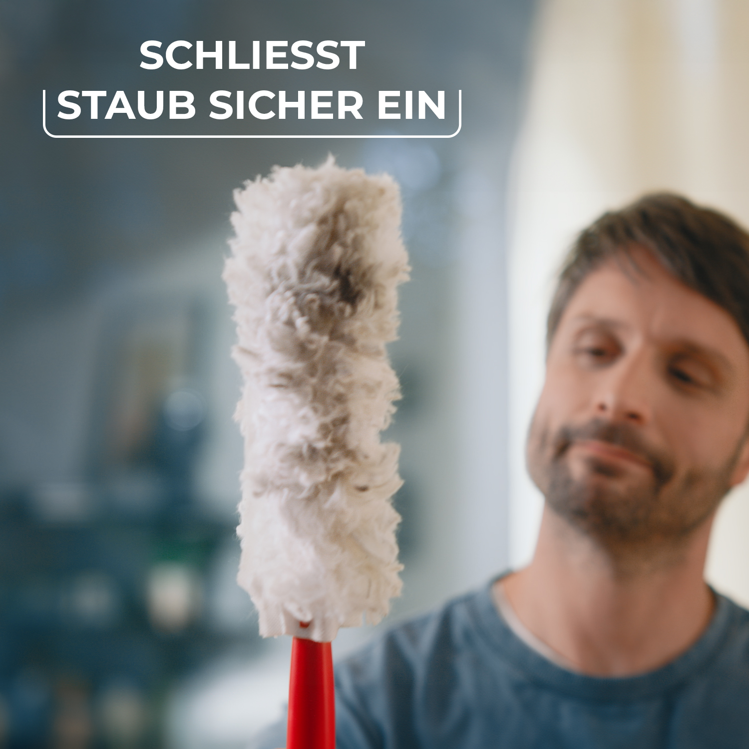 Ein Mann hält einen flauschigen grauen Staubwedel in die Höhe.