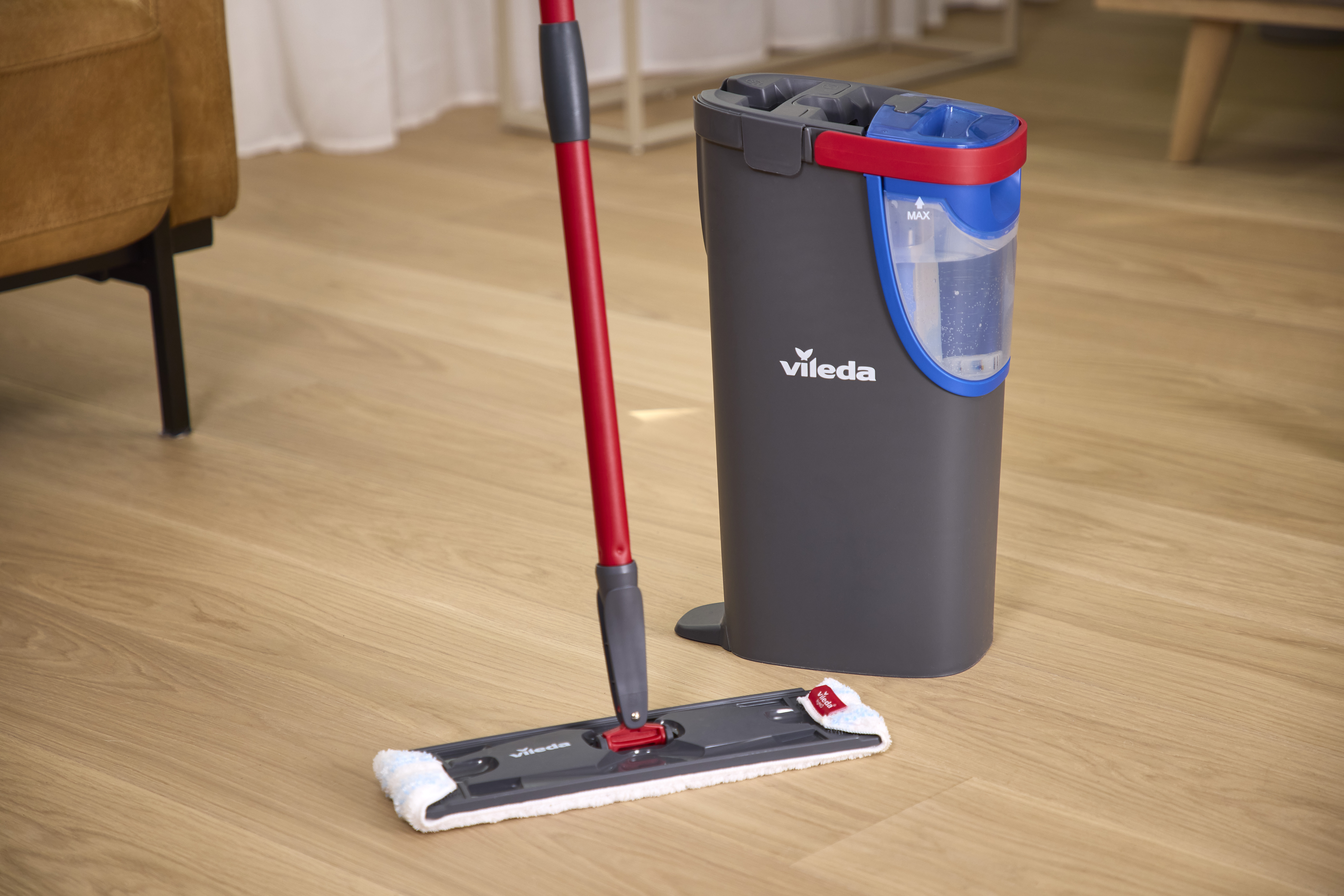 Ein Vileda Mop mit rotem Stiel und Eimer mit blauem Wassertank steht auf einem Holzfußboden.