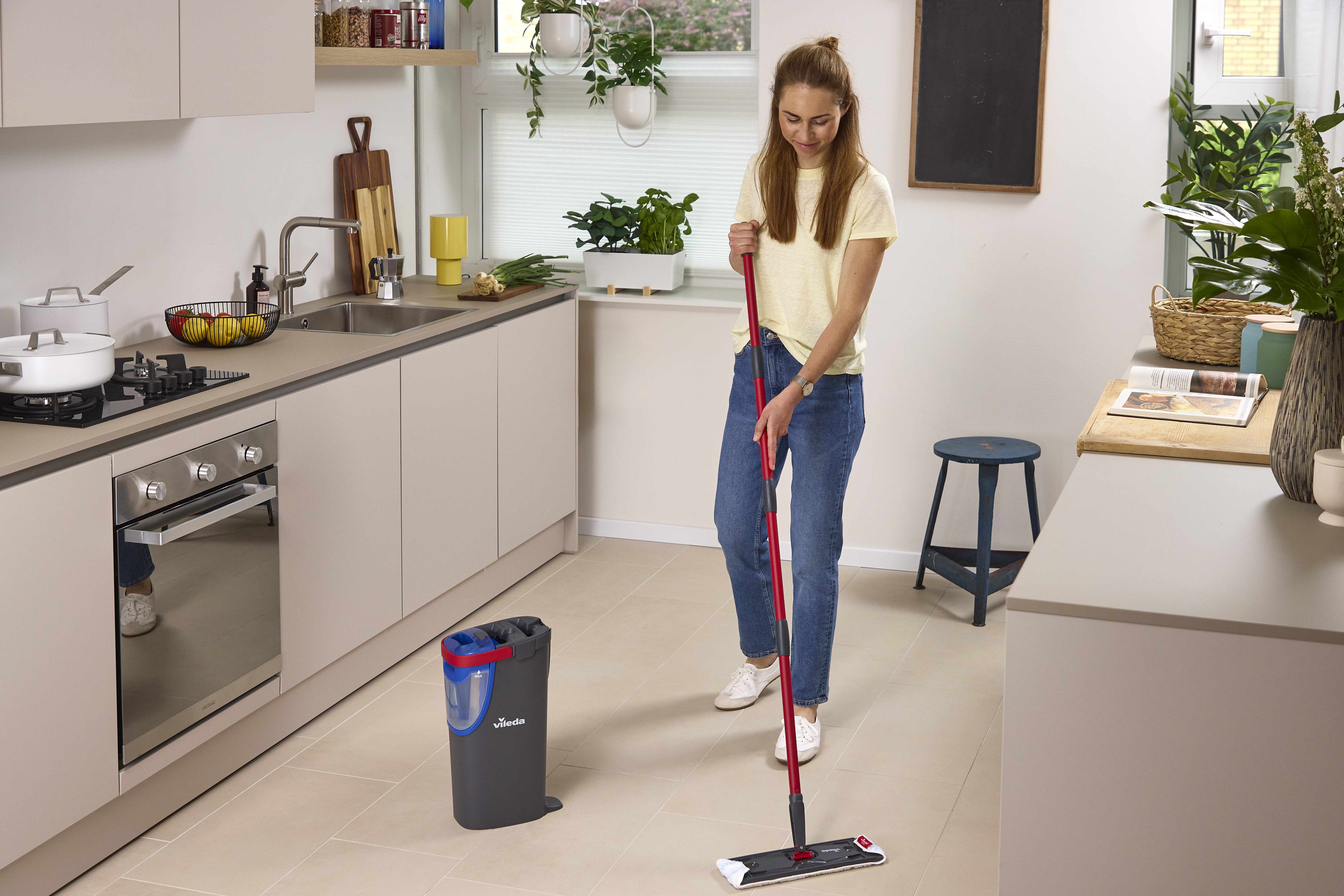 Eine Frau wischt den Küchenboden mit einem roten Vileda-Mopp und Eimer.