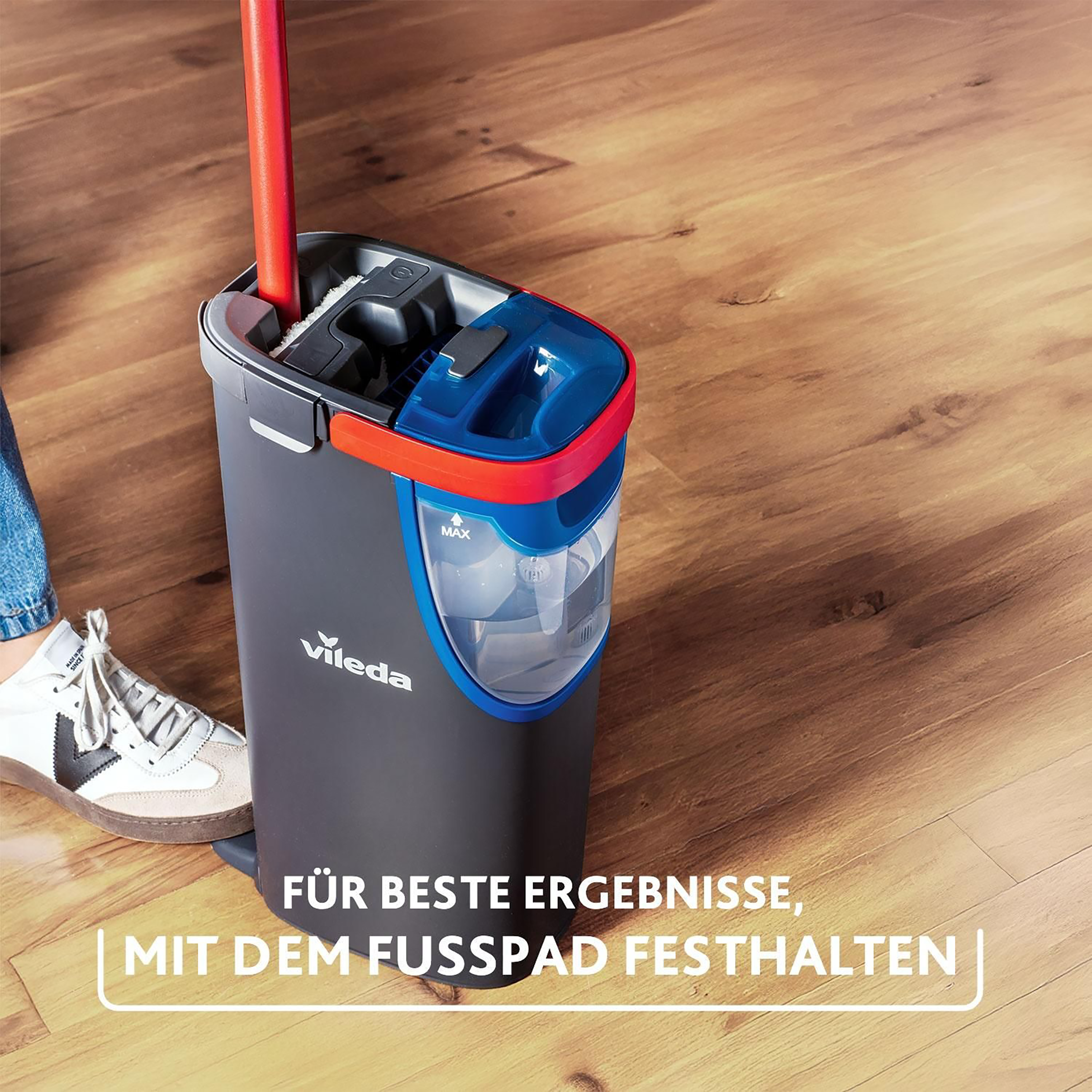 Ein Vileda Eimer mit rotem Griff steht auf einem Holzboden, ein Fuß hält ihn fest.