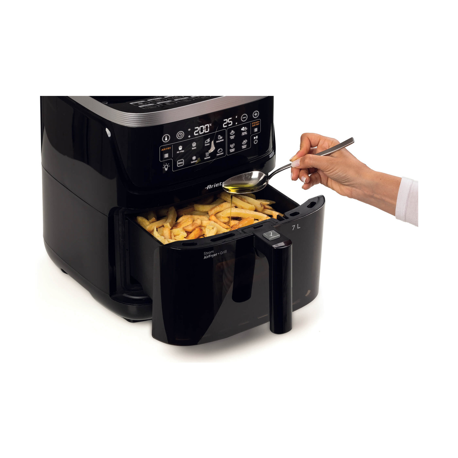 Una mano versa dell'olio con un cucchiaio sulle patatine fritte in una friggitrice ad aria nera.