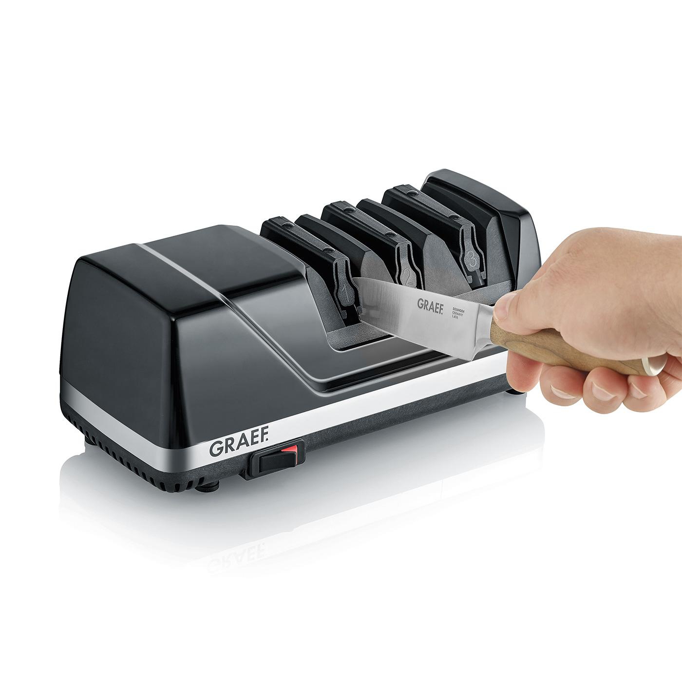 Eine Hand schärft ein Graef Messer in einem modernen schwarzen elektrischen Messerschärfer.