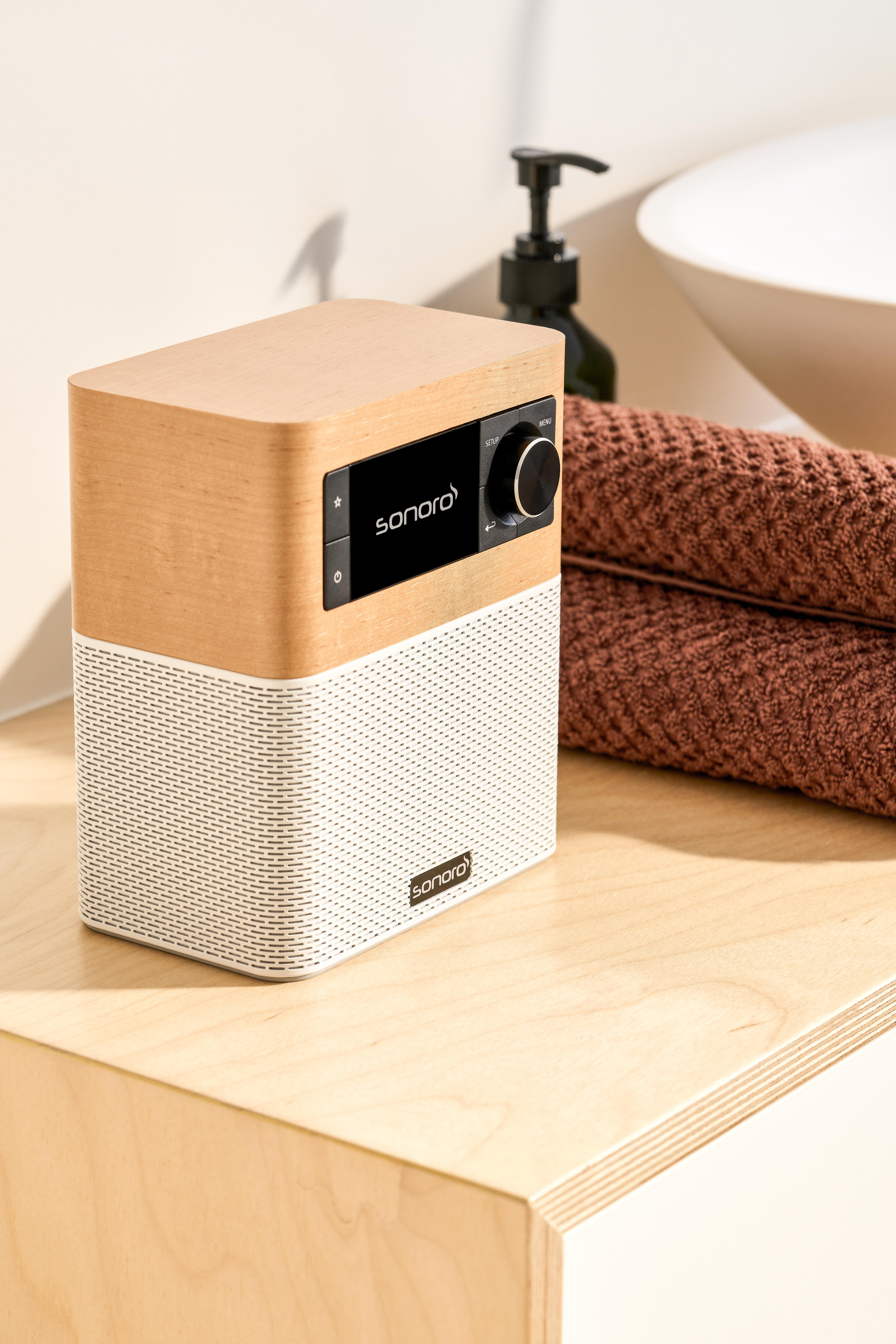 Ein hölzerner und weißer Sonoro Smart Speaker auf einer Theke neben braunen Handtüchern.