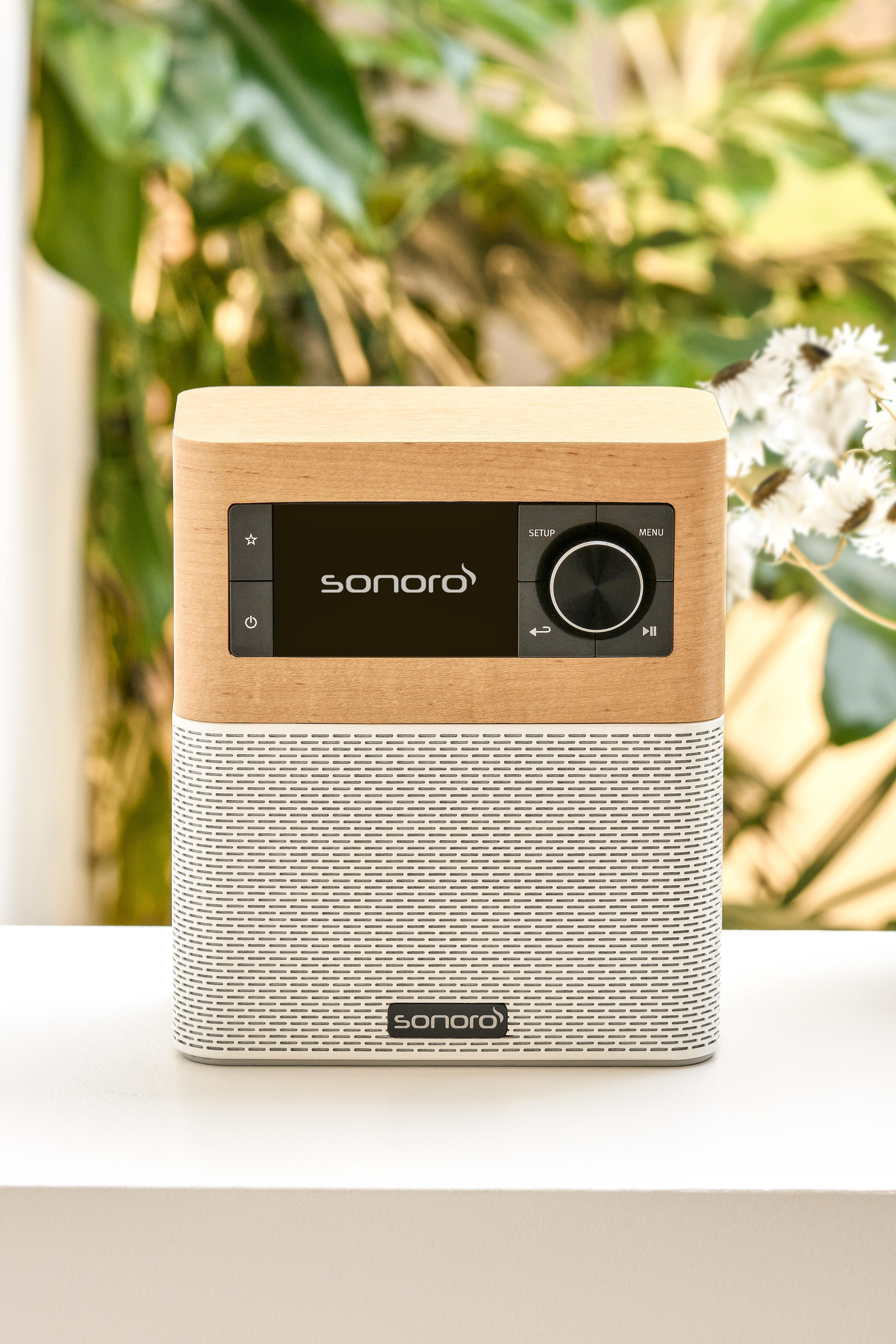 Ein Sonoro-Radio mit Holzverkleidung und weißer Lautsprecherfront steht auf einer weißen Oberfläche im Garten.
