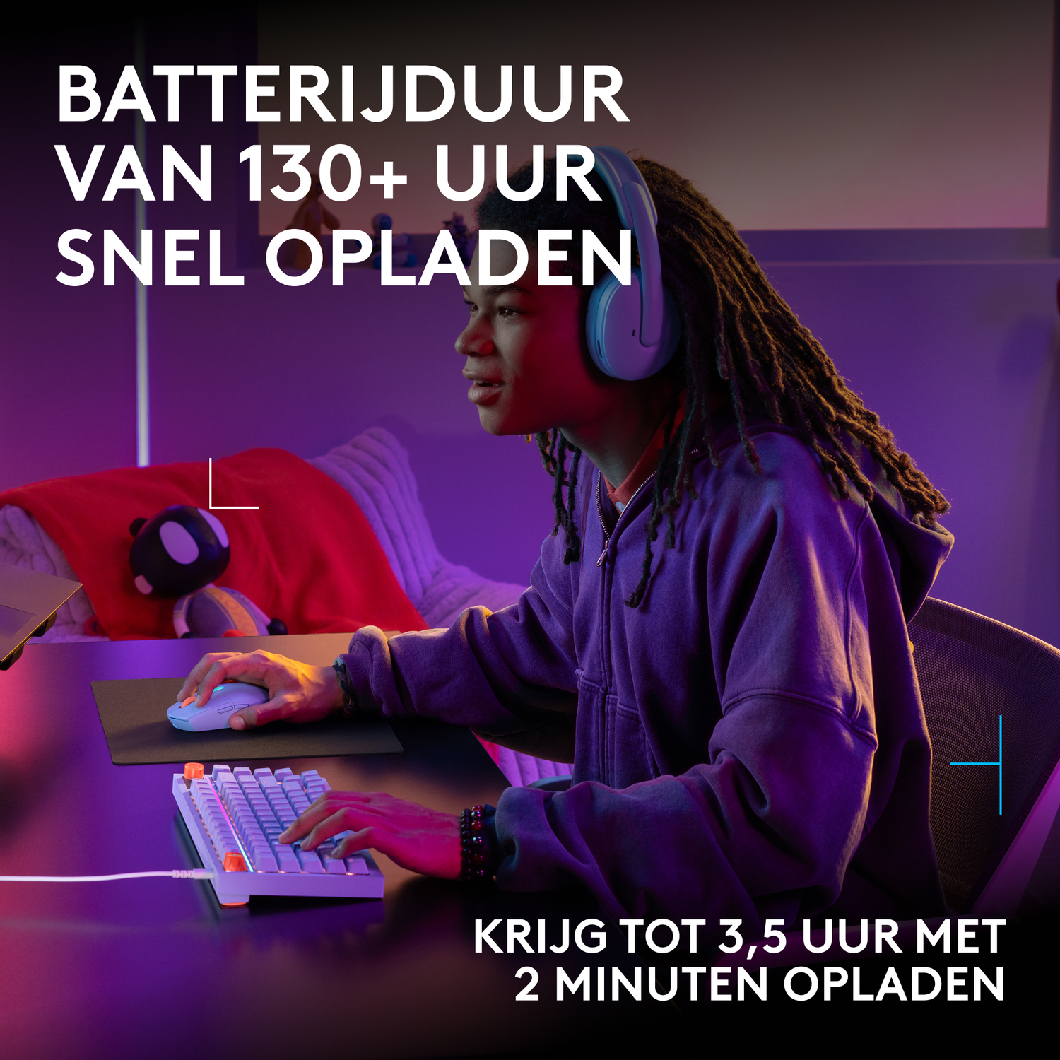 Een jonge man met dreadlocks en een blauwe koptelefoon gamet op een computer in een paars verlichte kamer.