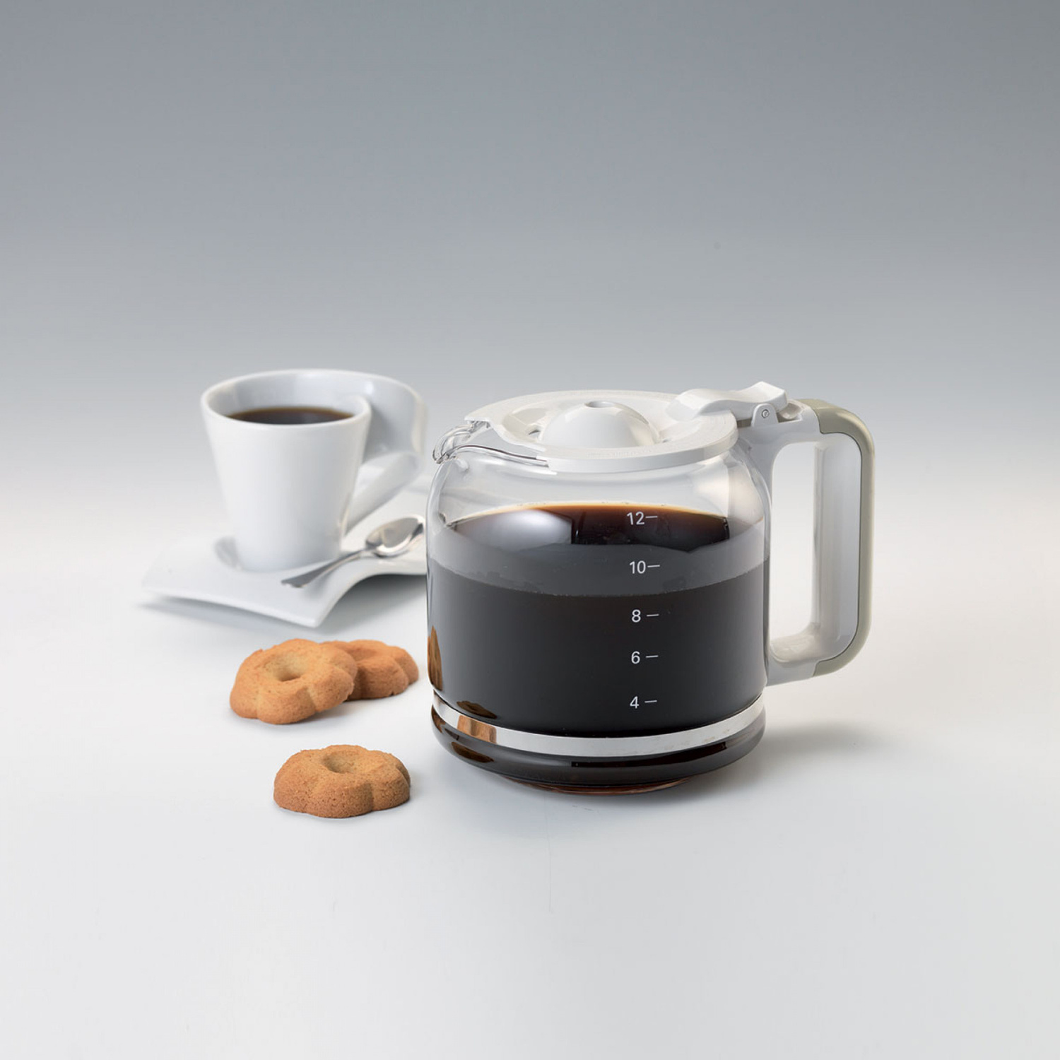 Una caffettiera di vetro con caffè scuro, una tazza bianca con cucchiaino e tre biscotti su fondo bianco.