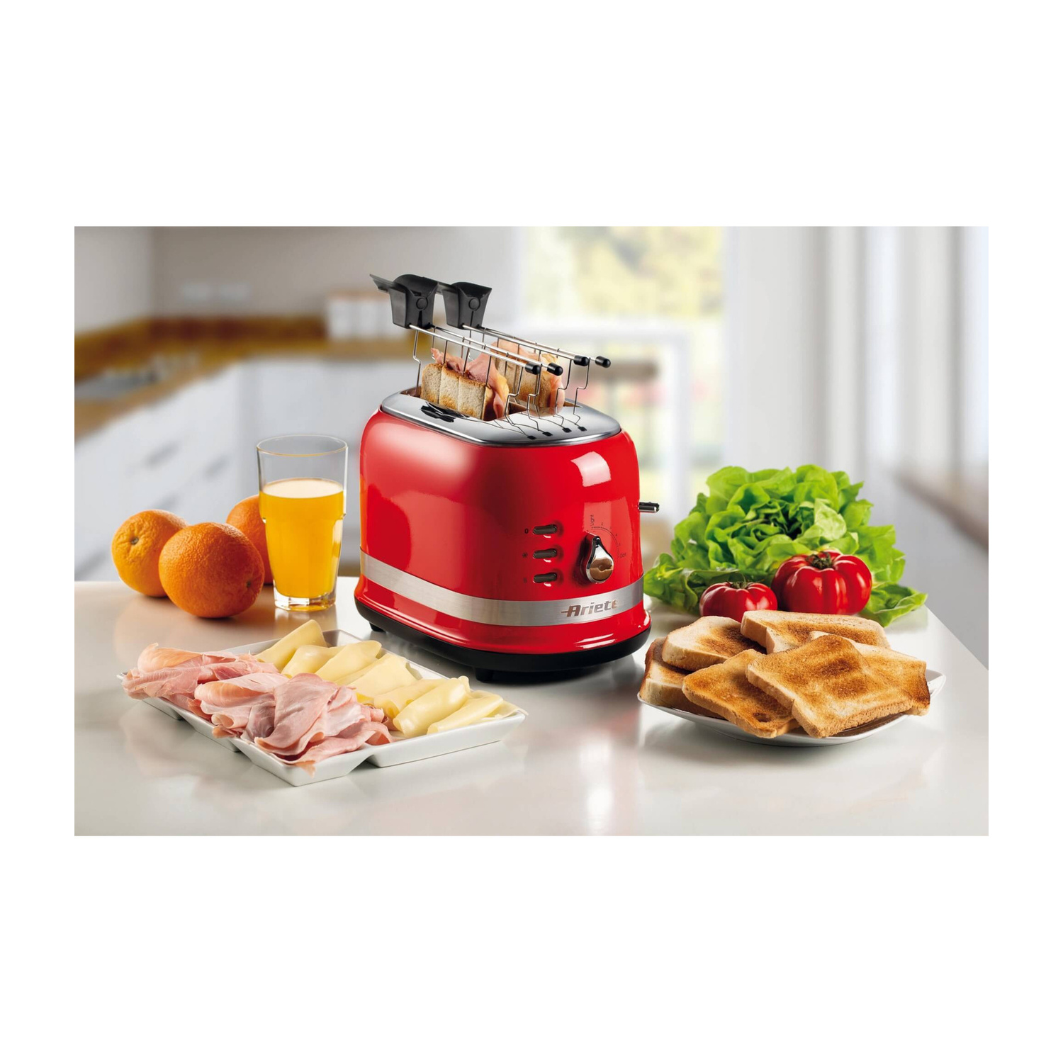 Un tostapane rosso su un tavolo da cucina con toast, prosciutto, arance e insalata.