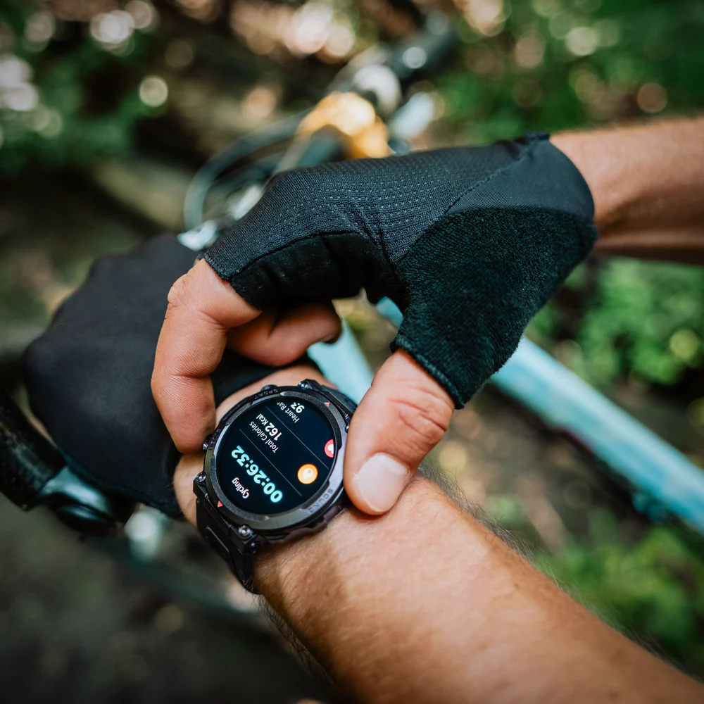 Fekete kesztyűs kerékpáros nézi a fitnesz okosórát az erdőben.