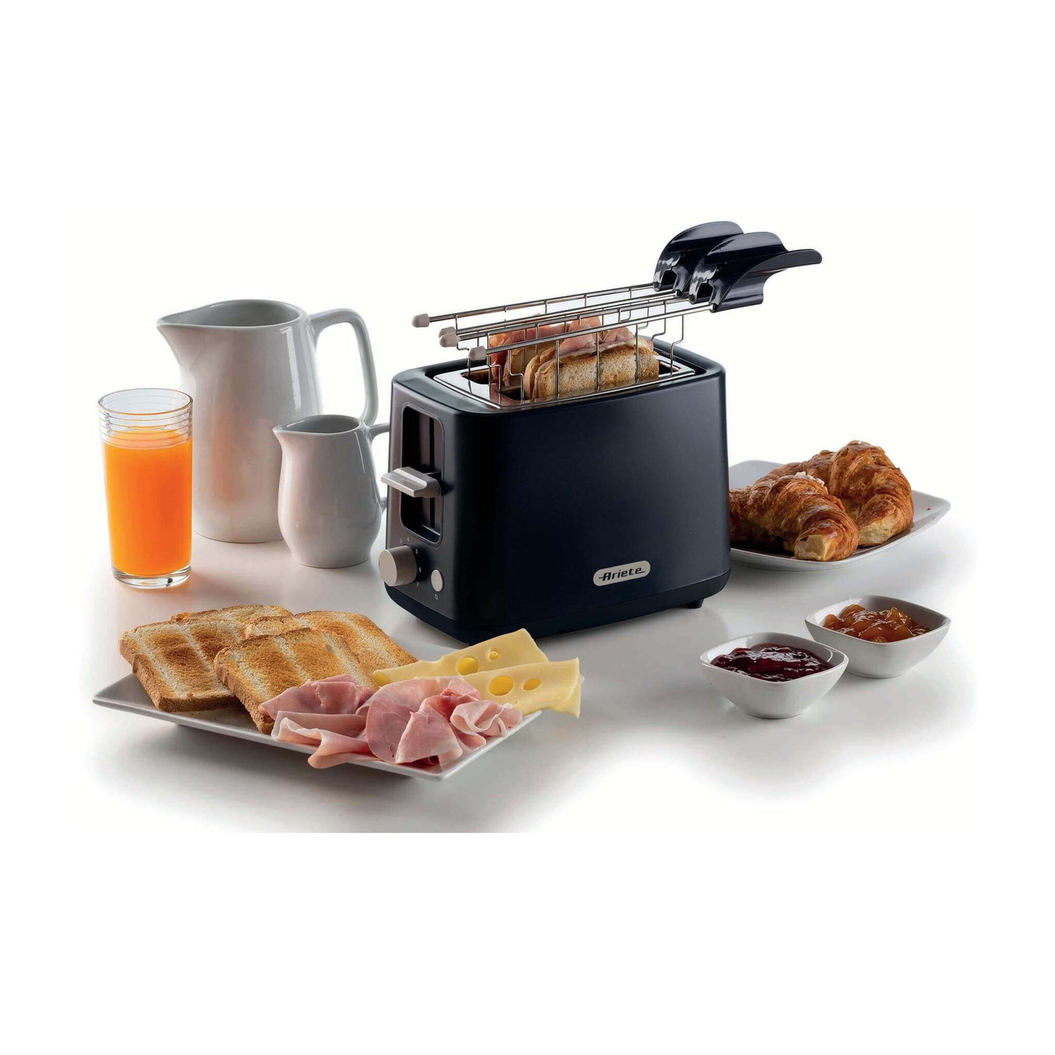 Un tostapane nero su un tavolo circondato da toast, prosciutto, formaggio, succo, croissant e marmellata.