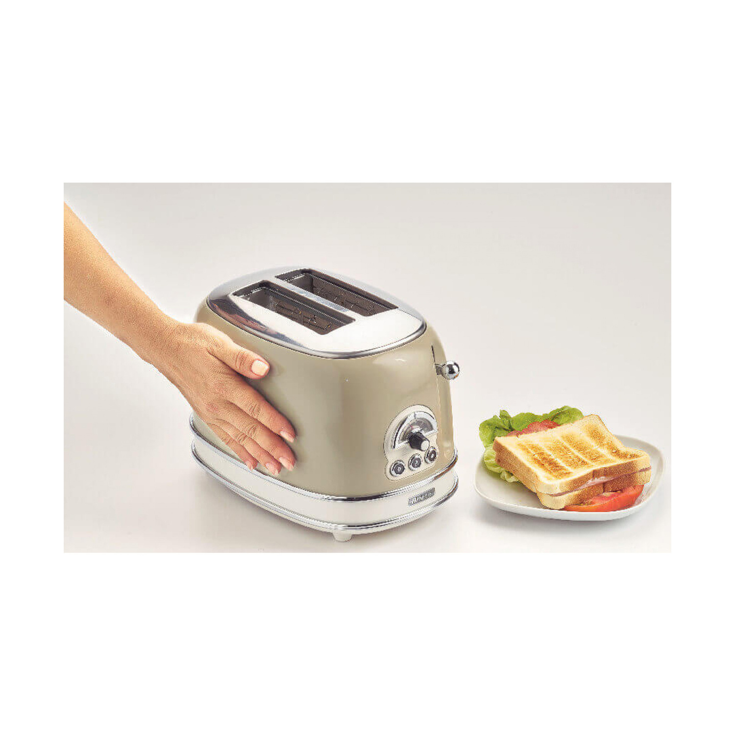 Una mano tocca un tostapane retro beige accanto a un piatto con un panino tostato.