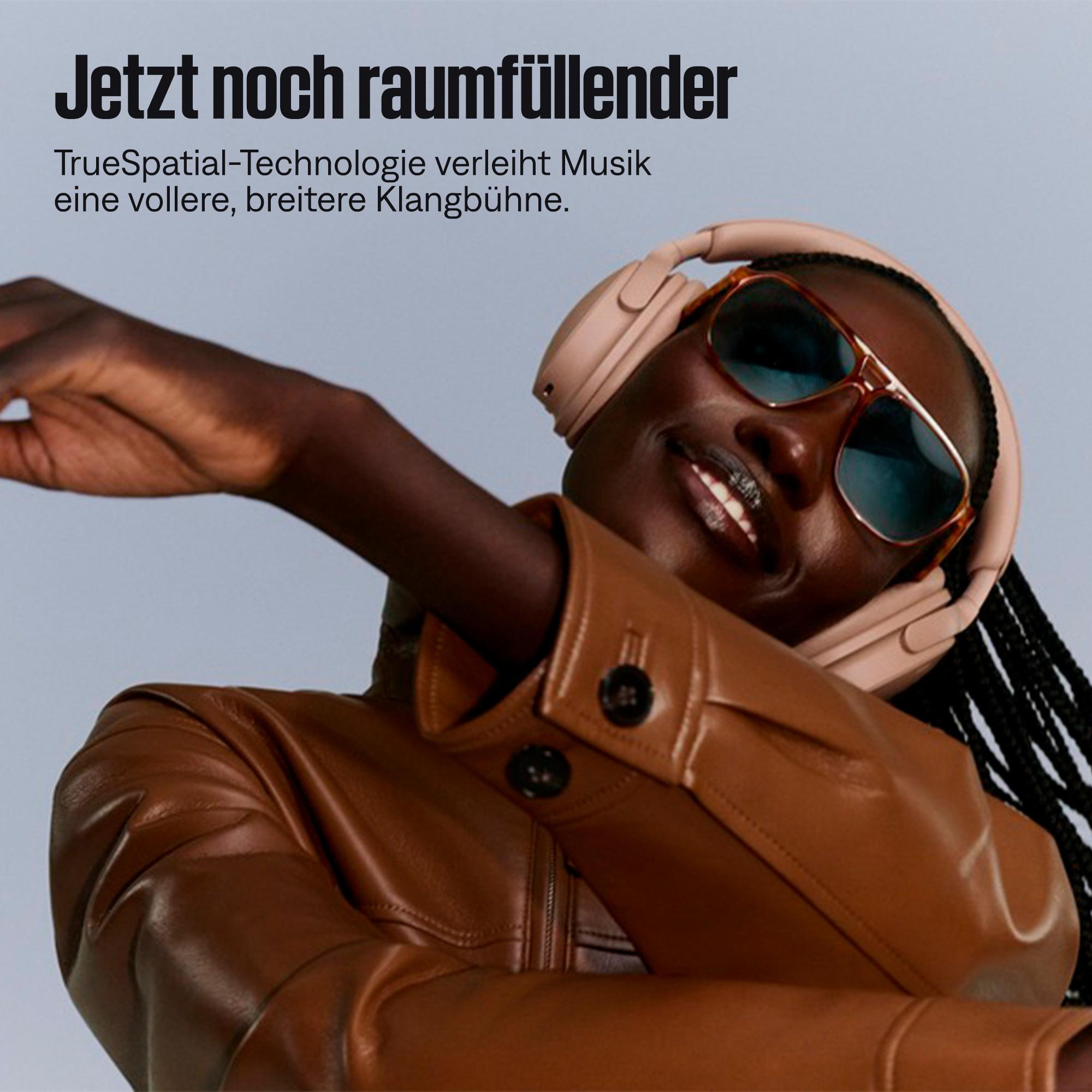 Eine Person mit rosafarbenen Kopfhörern und Sonnenbrille tanzt vor grauem Hintergrund.