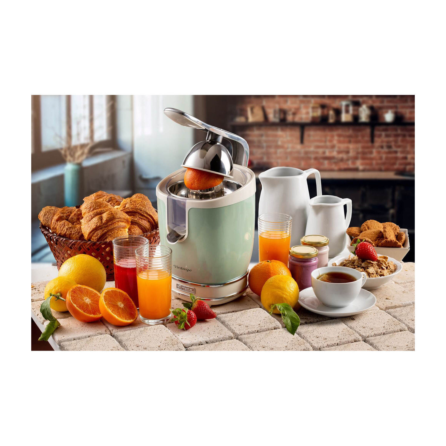 Un spremiagrumi verde menta è su un tavolo di pietra, circondato da croissant, succhi, frutta e tazze in una cucina.