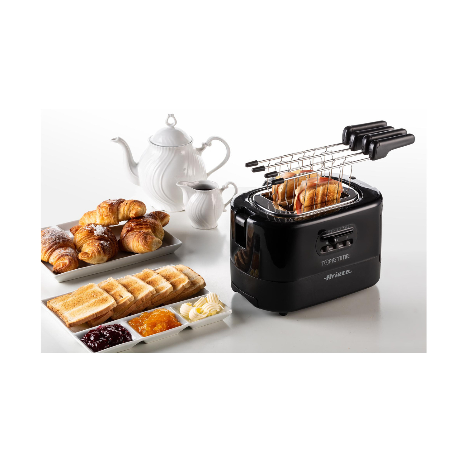 Un tostapane nero con toast, croissant, teiera e marmellata su un tavolo.