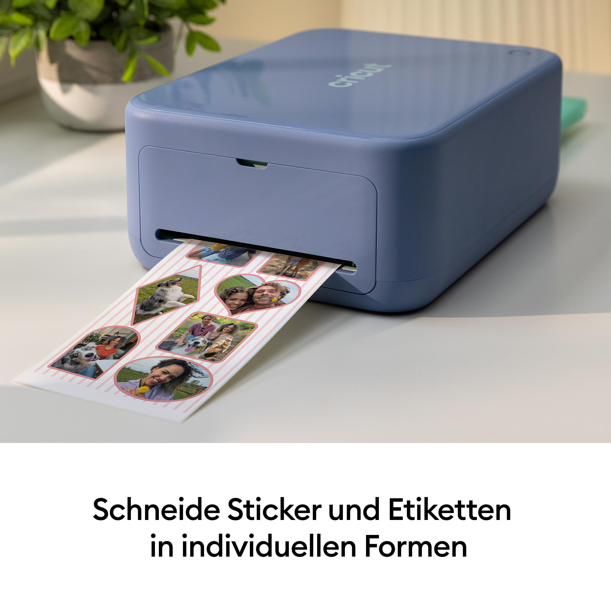 Ein blauer Cricut-Drucker auf einem Tisch druckt ein Blatt mit bunten Fotoaufklebern.